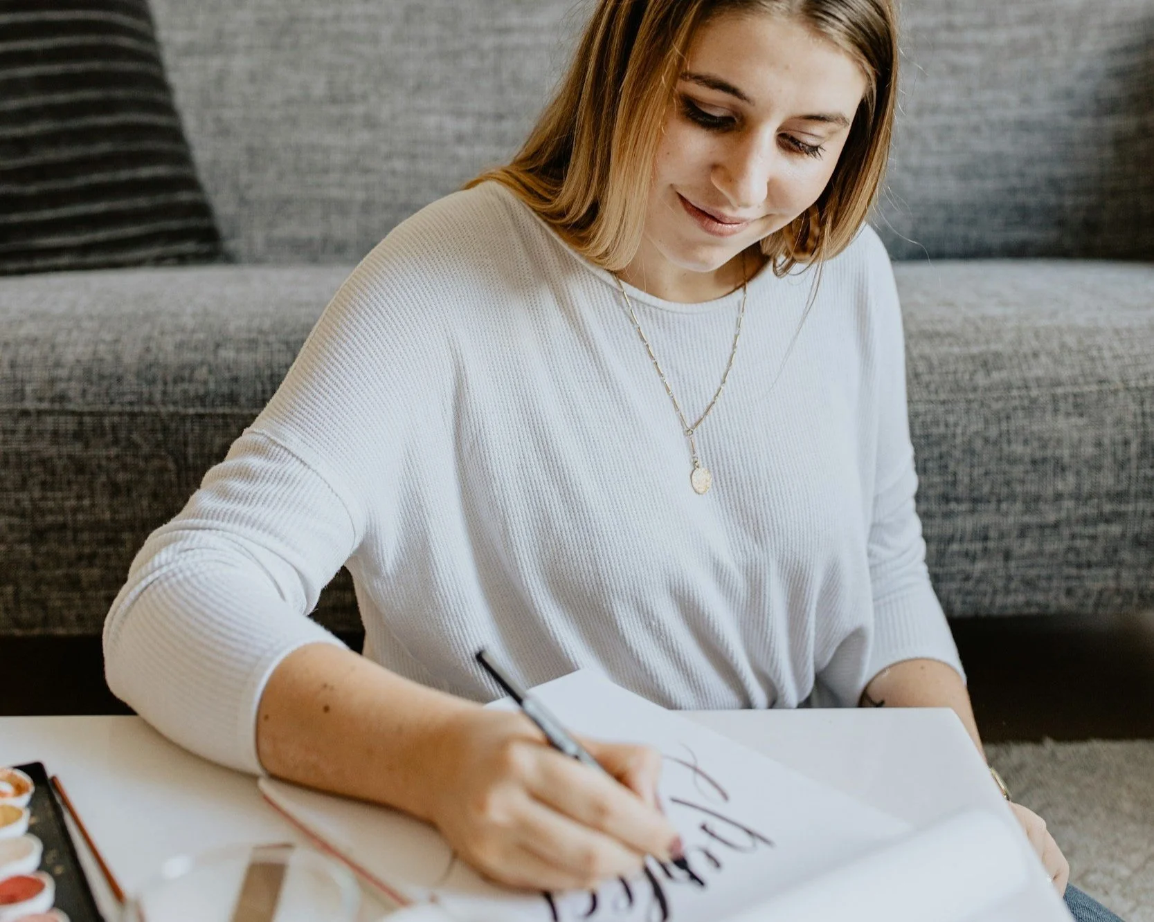 A smiling woman writing calligraphy with a brush pen.