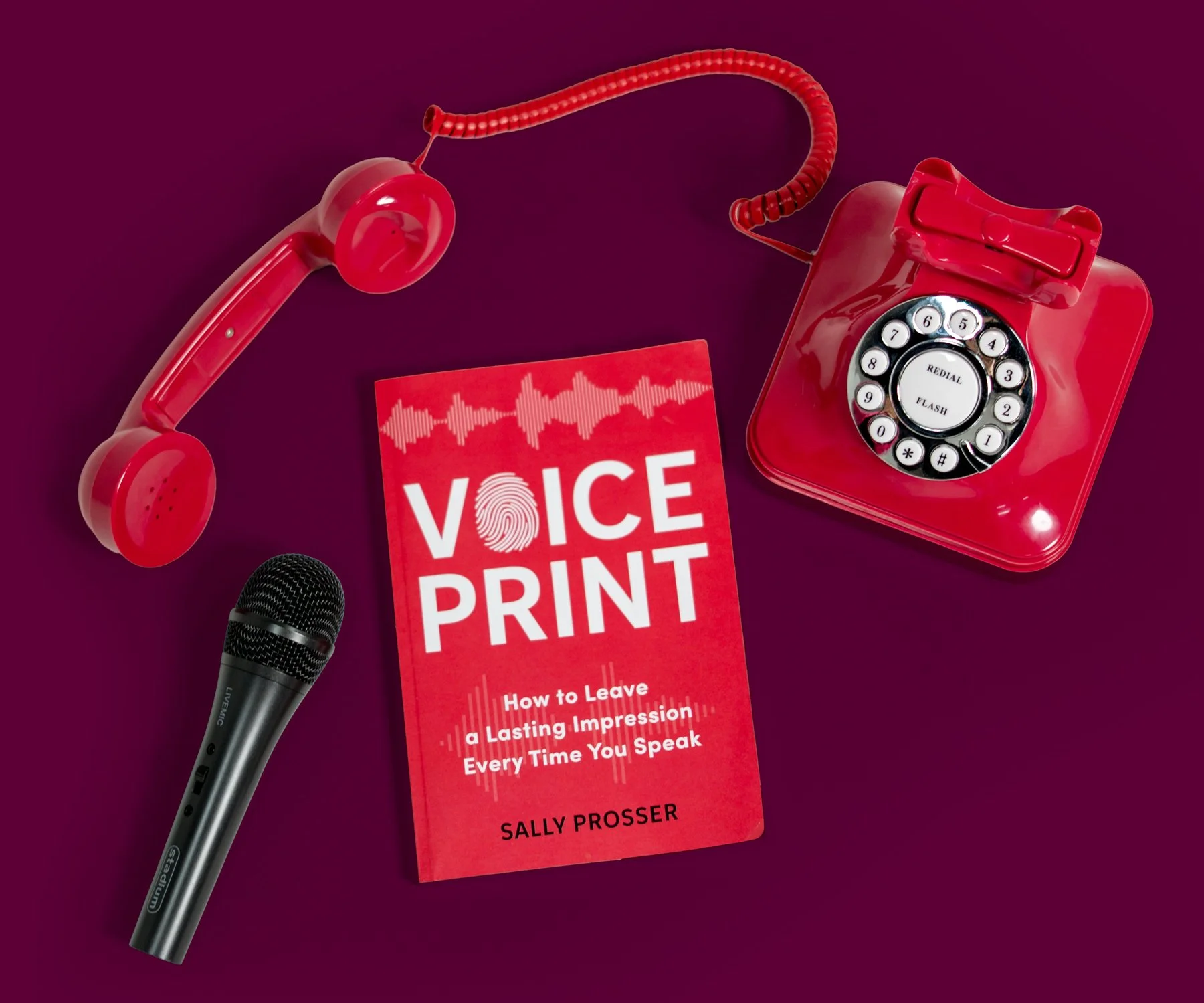 A red rotary phone, a black microphone, a book titled 'Voice Print: How to Leave a Lasting Impression Every Time You Speak' by Sally Prosser, all placed on a dark purple background.