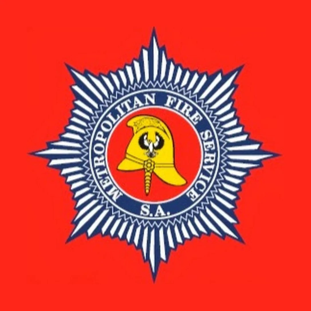 Emblem of the Metropolitan Fire Service, South Australia, featuring a firefighter helmet with a badge, surrounded by a starburst pattern on a red background.