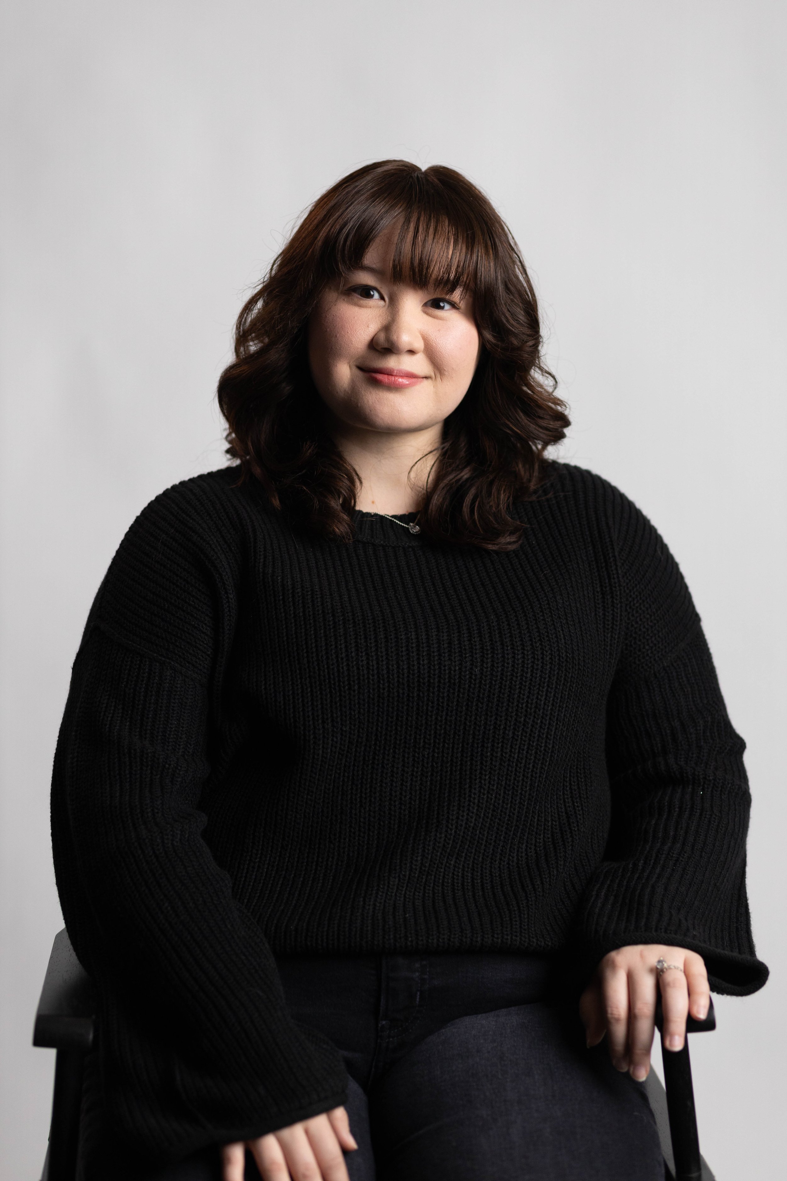 Amanda is sitting in front of a white backdrop dressed in all black.