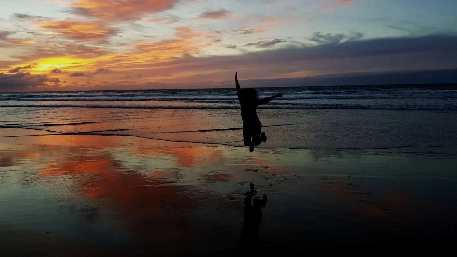 Silhouette of a person jumping joyfully on a beach at sunset, reflecting pain-free movement and active living supported by OrthoRub natural pain relief oil.