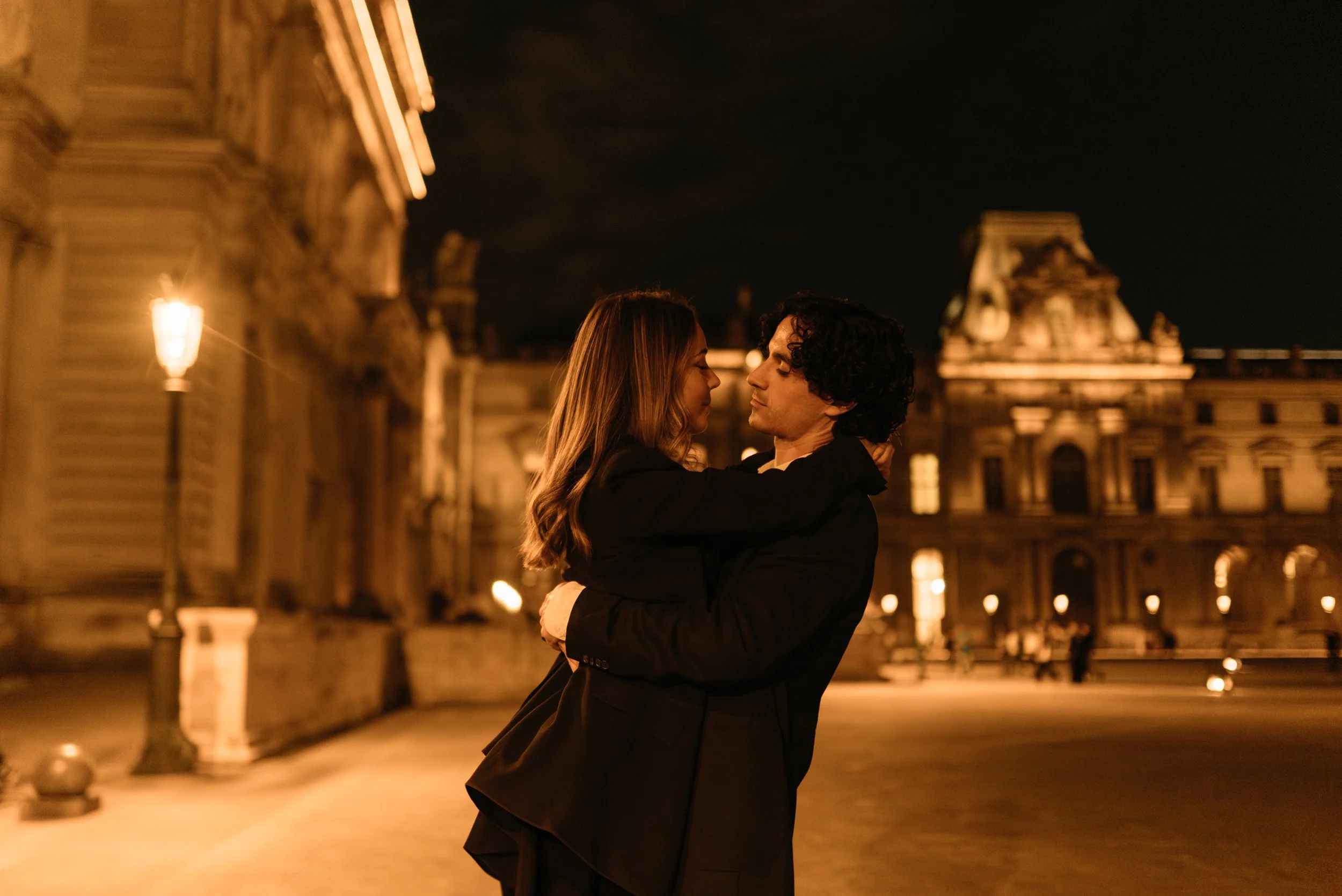 Un couple danse dans une ambiance nocturne à Paris, avec des bâtiments historiques et des lampadaires élégants en arrière-plan.