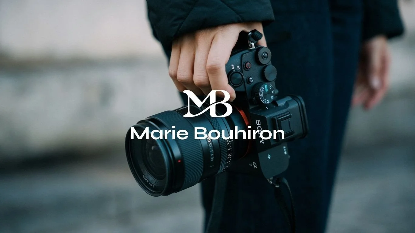 Une personne tient un appareil photo numérique avec un objectif amovible dans sa main, portant un manteau noir.