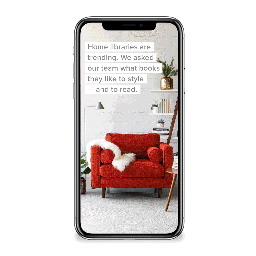 Smartphone screen displaying a living room with a red armchair, a white fluffy throw, a small side table, potted plants, and wall shelves with books and decor. Text overlay reads: "Home libraries are trending. We asked our team what books they like to style — and to read."