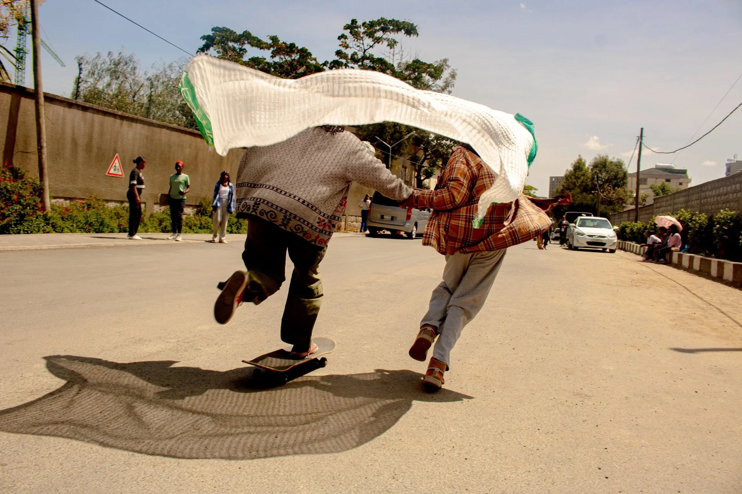  Two girls hold a traditional Ethiopian cloth called a ‘netela’ while one of them holds another riding a skateboard in Addis Ababa, Ethiopia on February 24, 2024. The girls are a part of an all girl skating group called ‘Ethiopia Girls Skate’. It is 