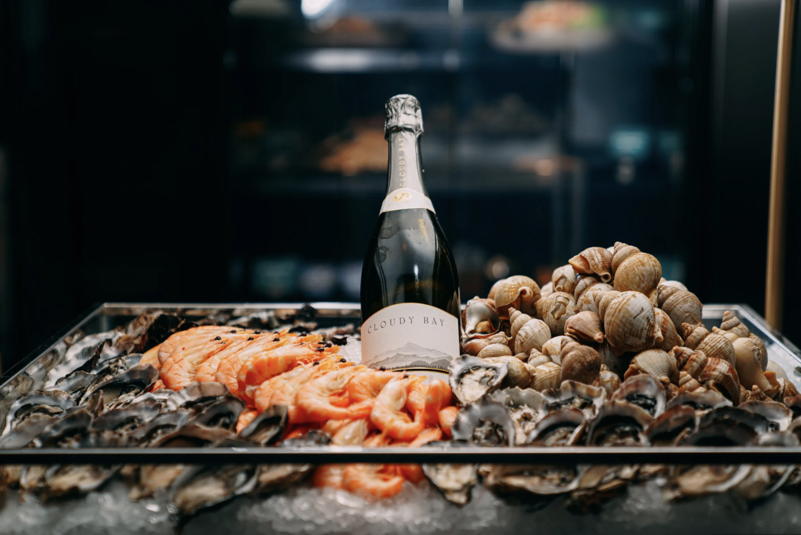 A tray of fresh seafood including oysters, salmon, and clams, with a bottle of Cloudy Bay wine in the center.
