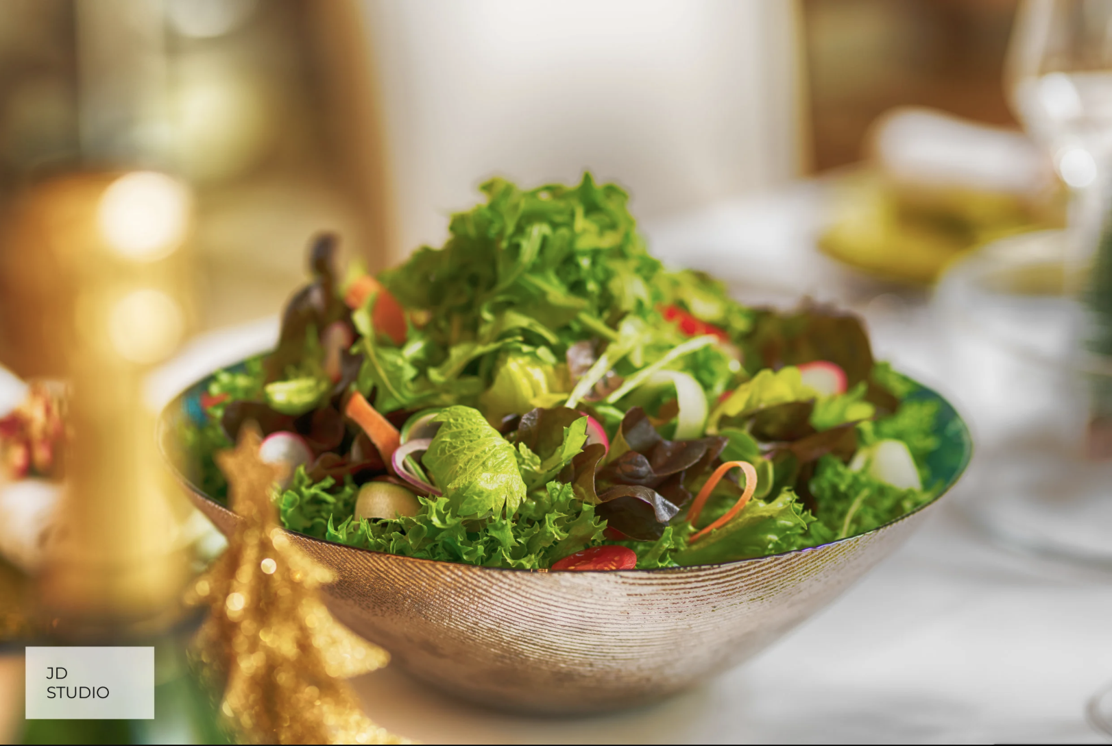 A colorful bowl of fresh mixed salad on a table, with blurred holiday decorations and tableware in the background.