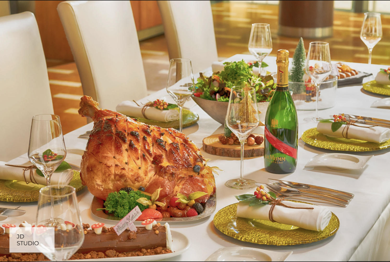 A holiday feast on a dining table with a roasted ham as the centerpiece, surrounded by salad, desserts, champagne, and beautifully set place settings with napkins and glassware.
