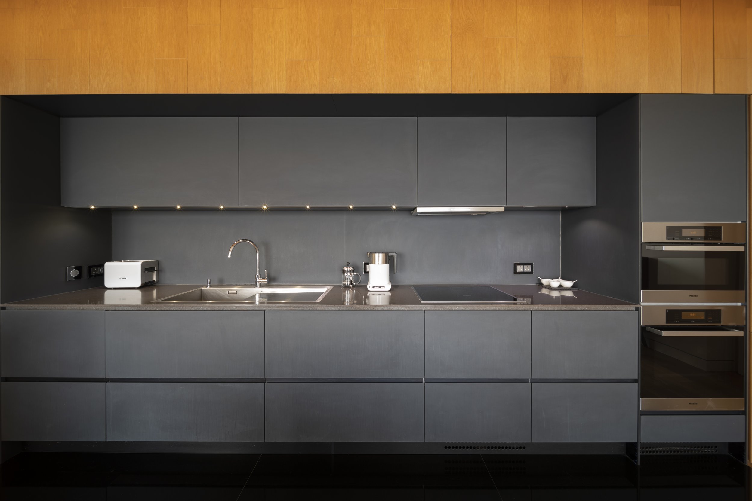 Modern kitchen with dark gray cabinetry, built-in oven and microwave, stainless steel sink, and small appliances on the countertop.