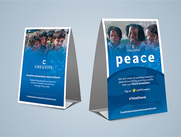 Two table top folded event displays featuring images of smiling children and text about supporting global positive change.