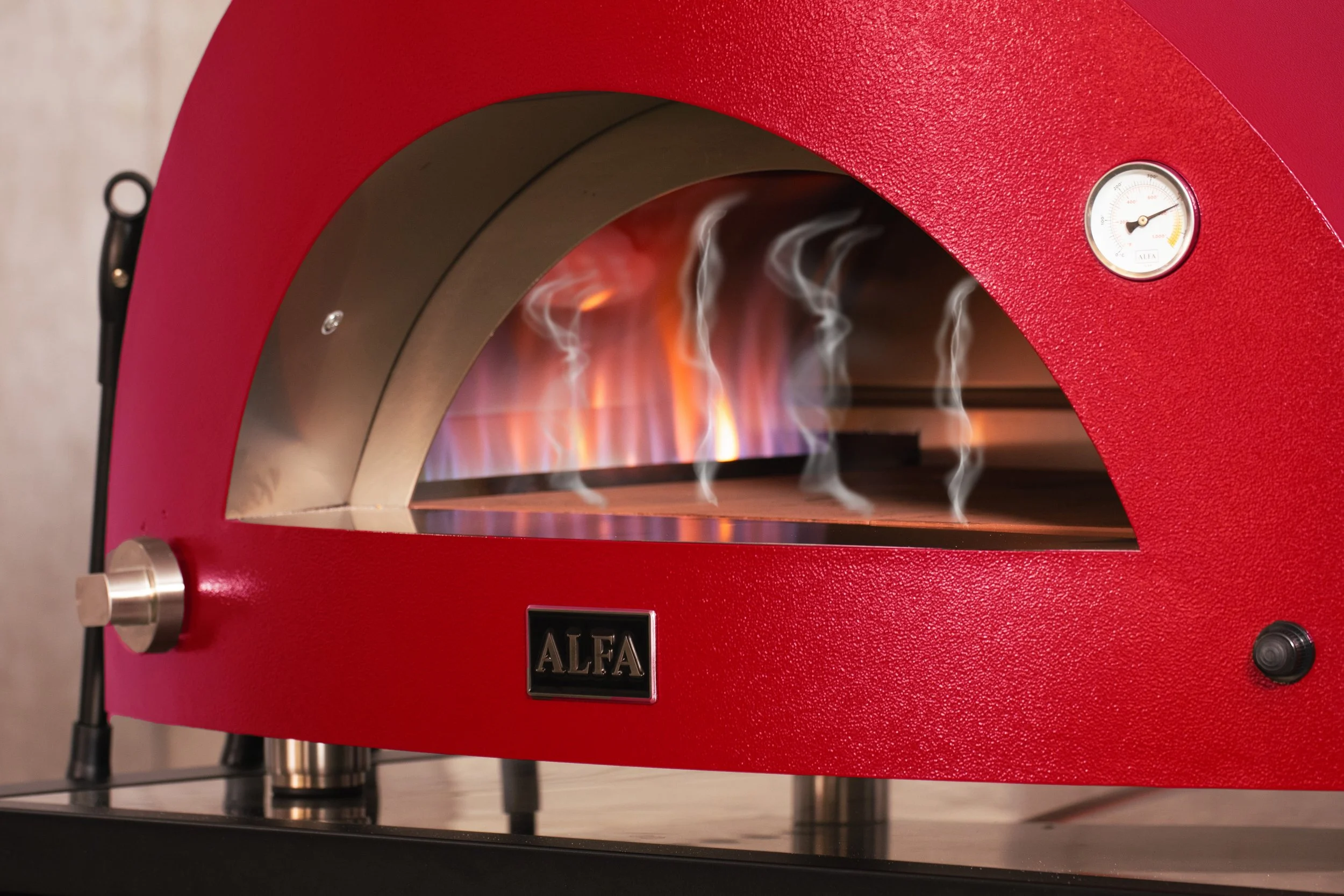 Röd pizzaugn med ett fönster där brinnande eld syns och en termometer på utsidan.