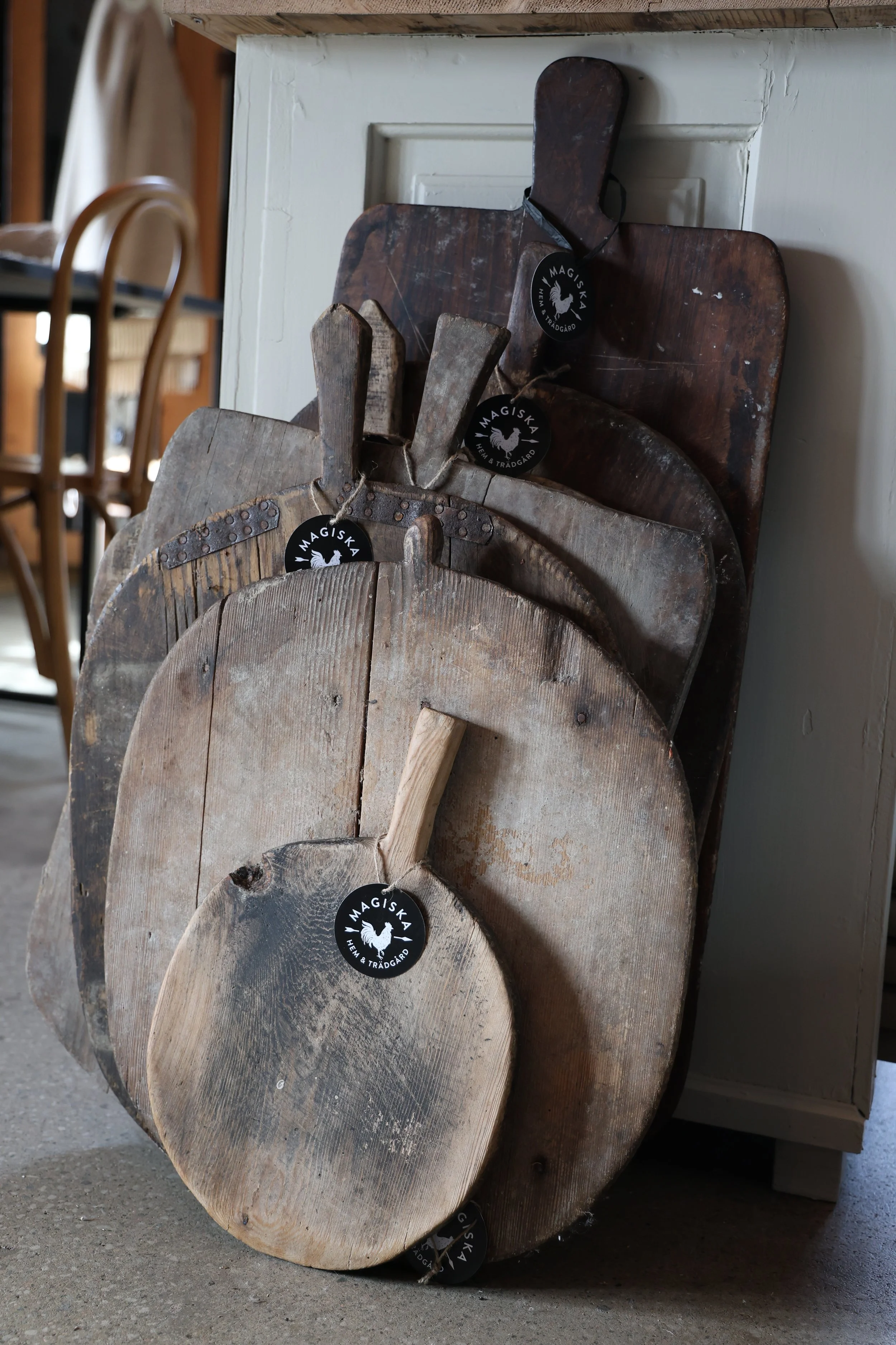 Flera gamla träskärbrädor staplade mot en vägg, märkta med etiketter som säger 'Magiska Hem & Trädgård'.