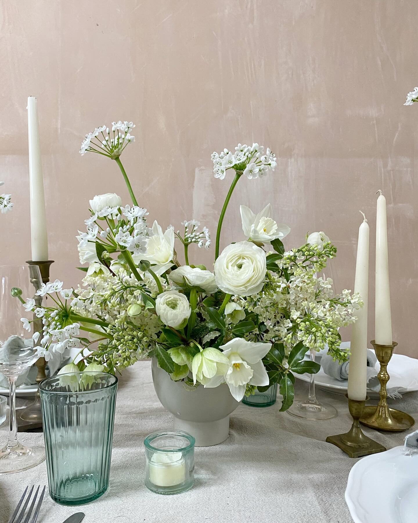 Whites and greens look gorgeous in any season, this spring bowl arrangement includes a mix of blousy ranunculus, beautifully scented lilac, dainty alliums, and perfect ivory narcissus. Mixed with tall taper candles in brass candlesticks and lots of t