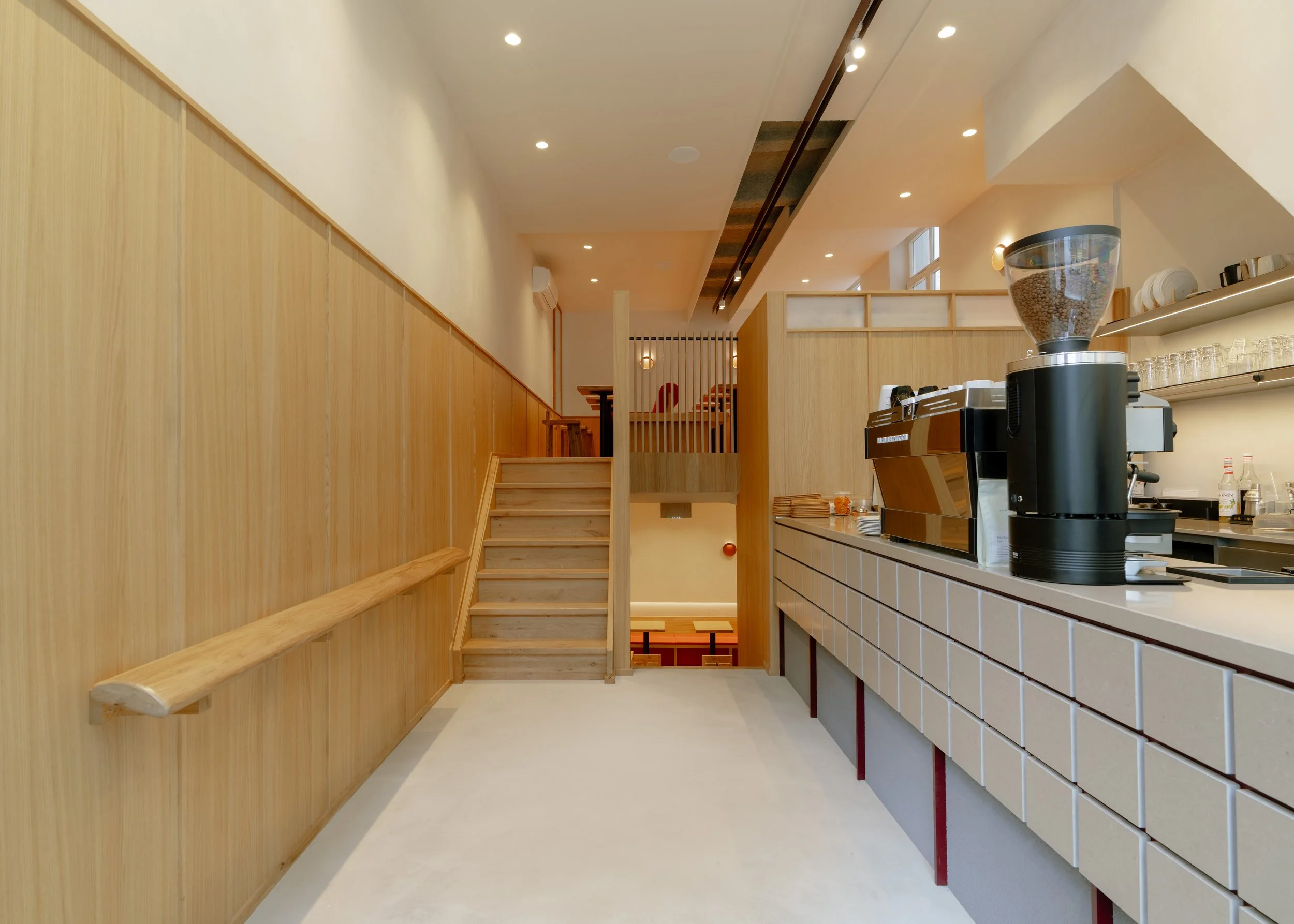 Interior of a modern cafe or restaurant with wooden paneling, a staircase, and a counter with coffee equipment.
