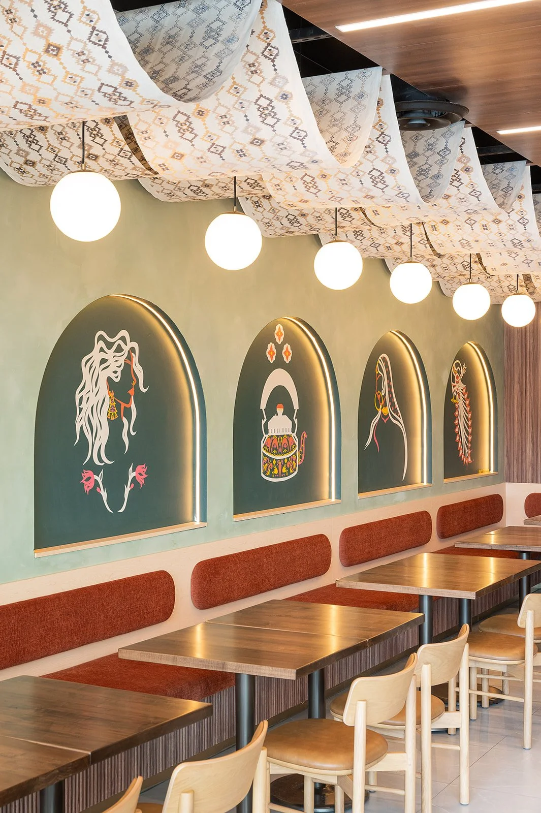 Burnt orange banquette with walnut woods, sage lime wash walls, and overhead fabric installation