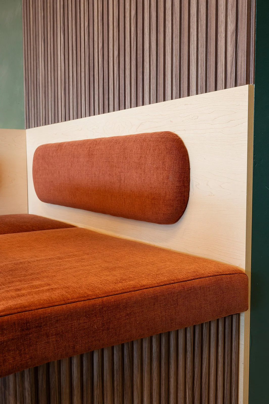 Close-up of custom restaurant booth seating with rust-orange upholstered cushions, light wood backing, and vertical wood slat detailing.