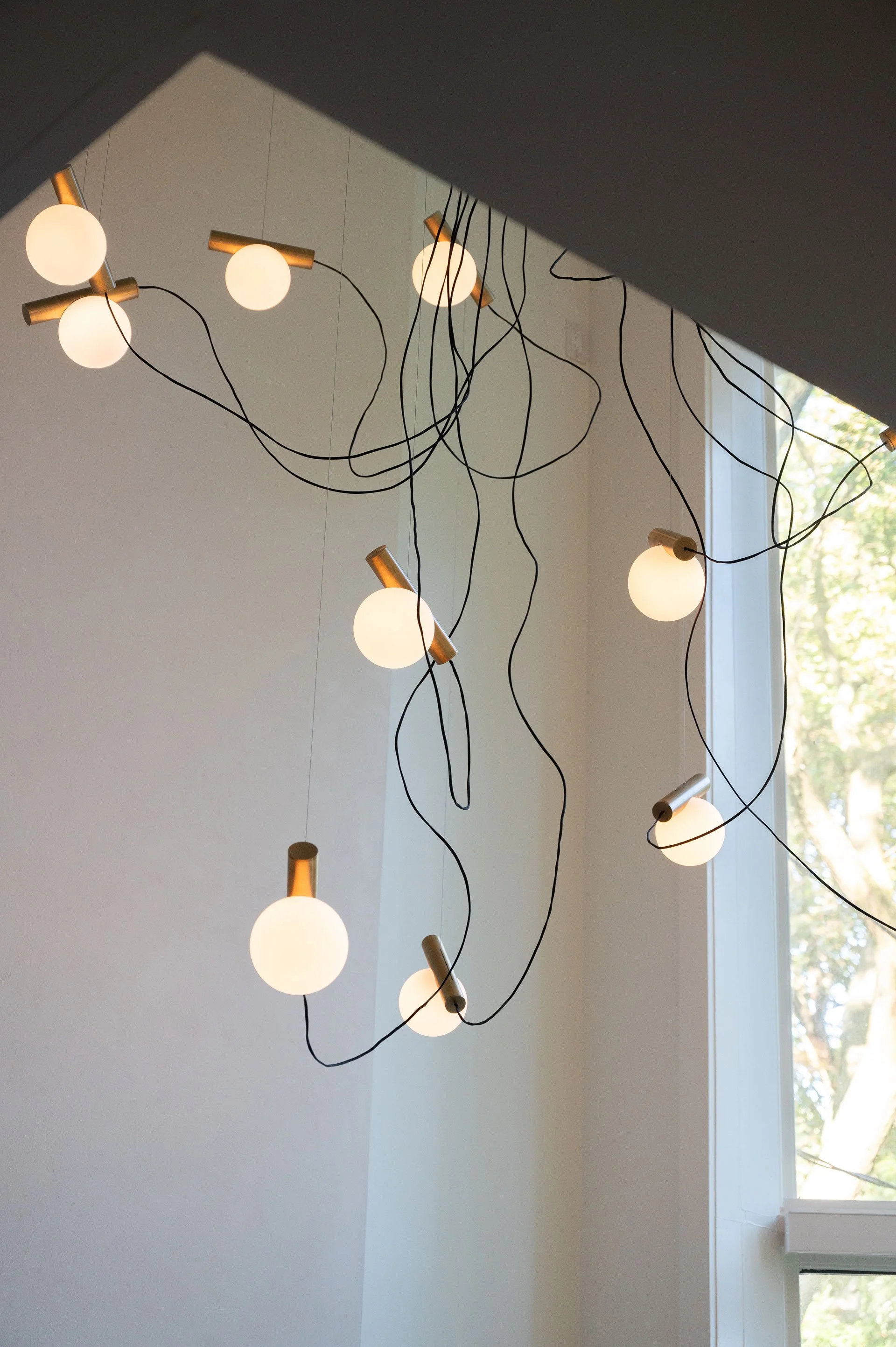 Chandelier with warm lit globes with a cylinder gold accent attached to black wires to appear floating