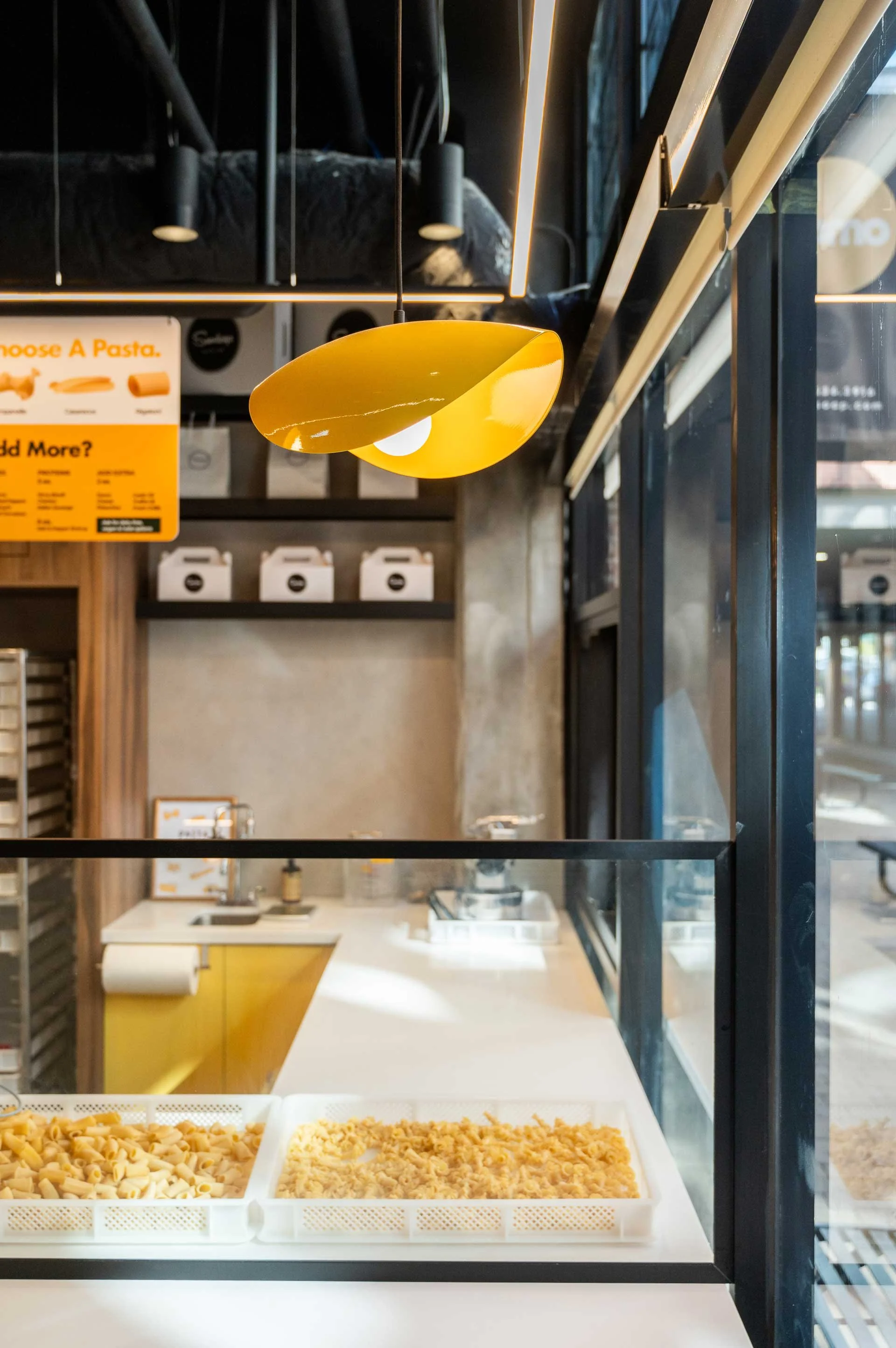 Yellow pasta noodle pendant light above a white quartz counter with a black frame sneeze gaurd