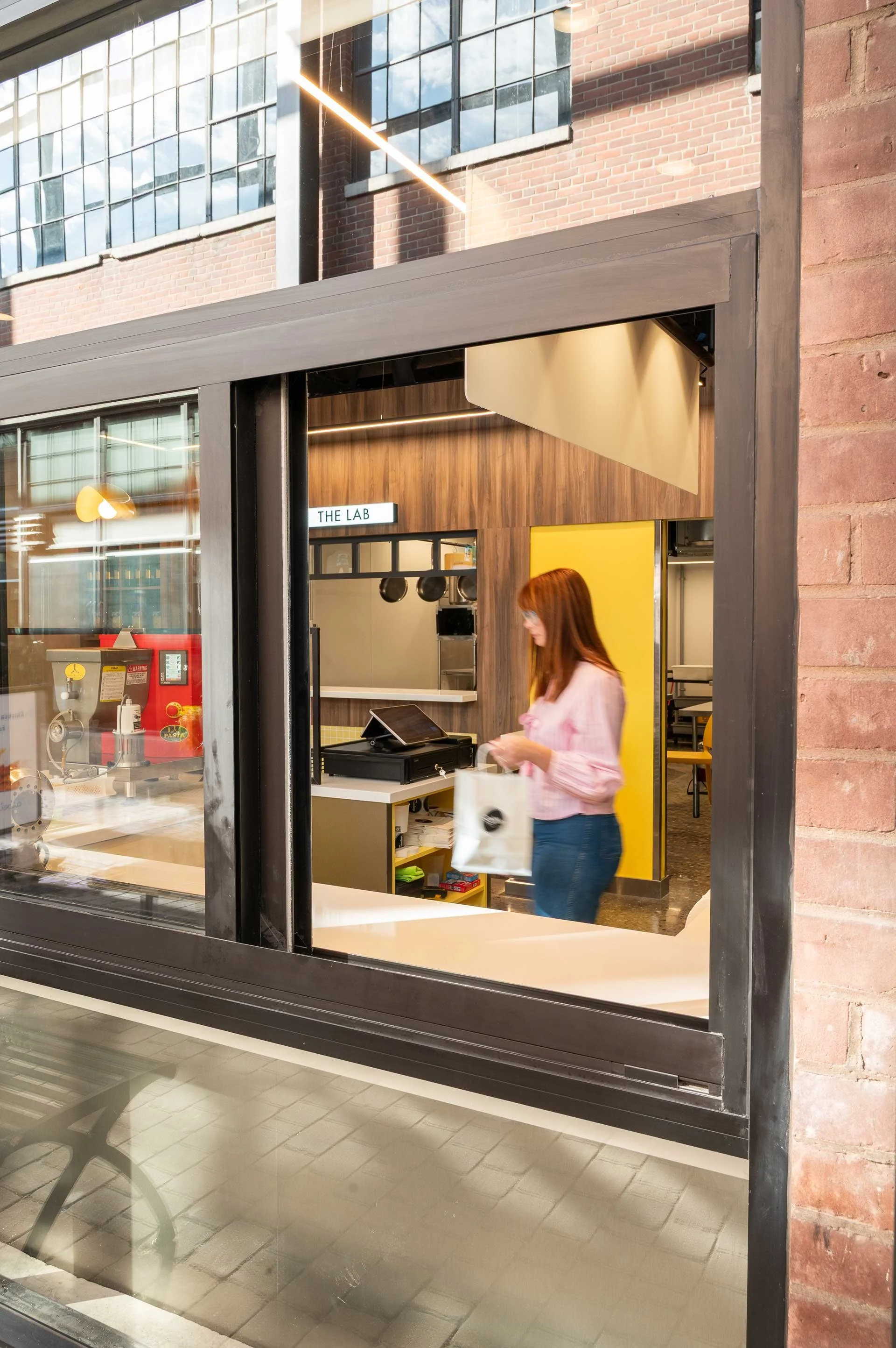 pass through window looking into a pasta restaurant with a lady holding a white takeout bag