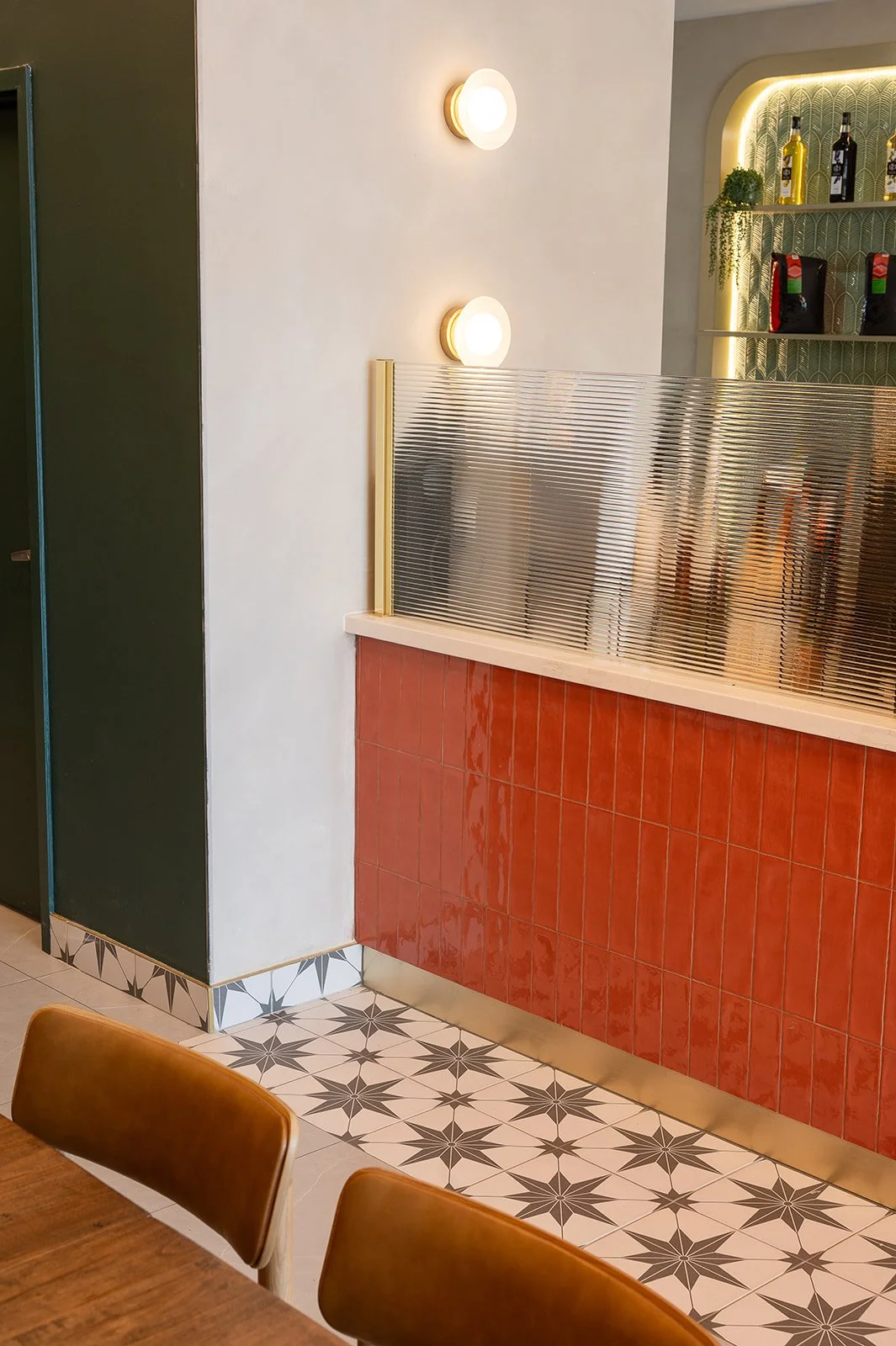 Modern cafe interior featuring an orange tiled counter, fluted glass privacy divider, star-patterned floor tiles, and tan leather dining chairs.