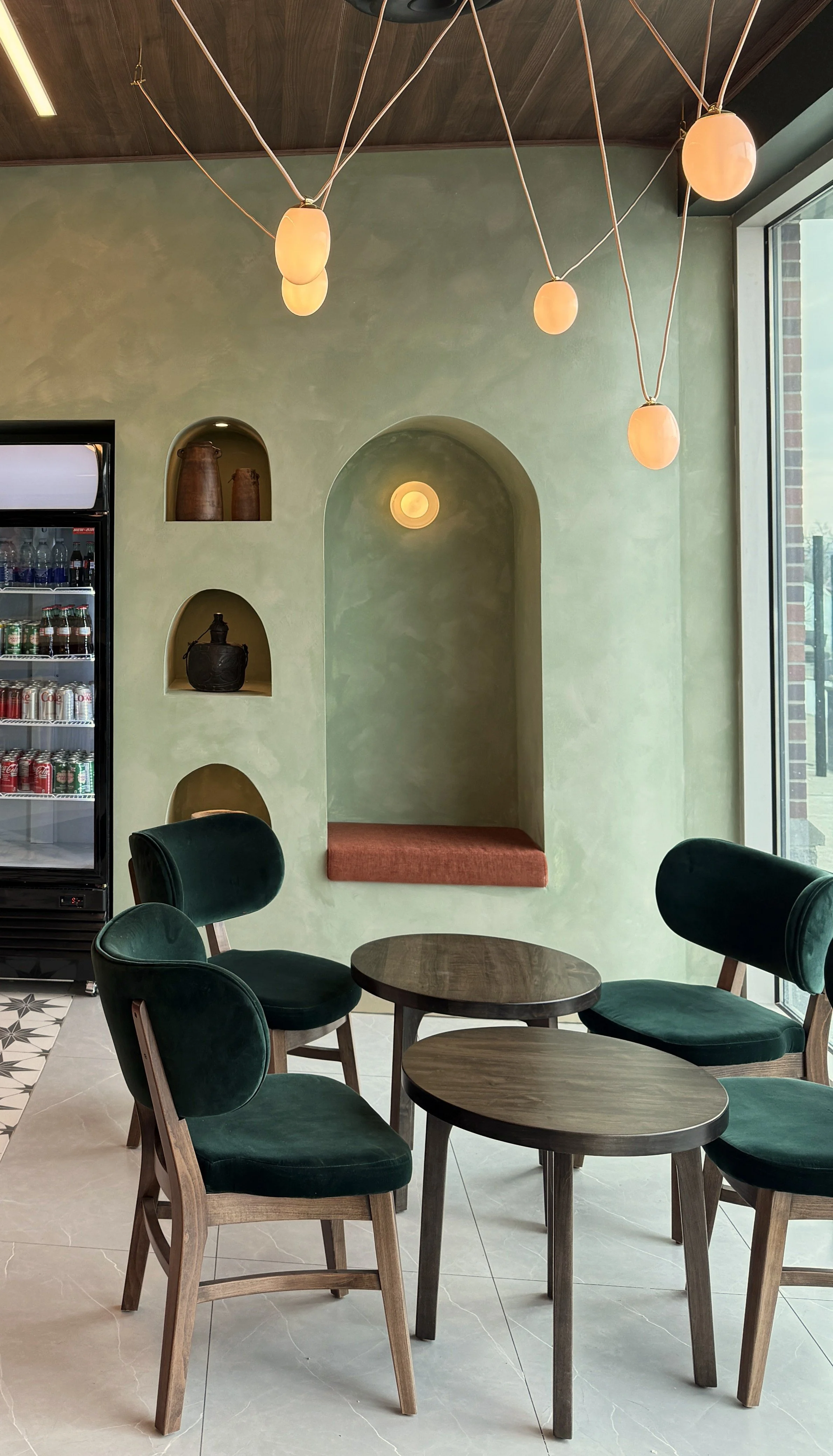 Green velvet chairs positioned for relaxed coffee experience, with limewash wall niches behind