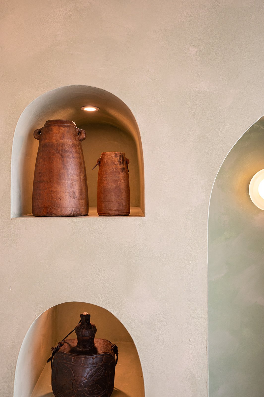 Limewash wall with arched niches displaying terracotta pottery vases