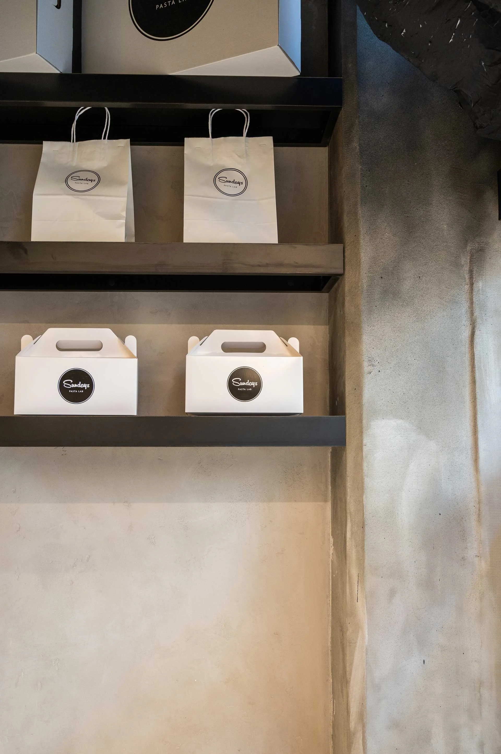 concrete walls with black metal floating shelf with various white takeout boxes and bags