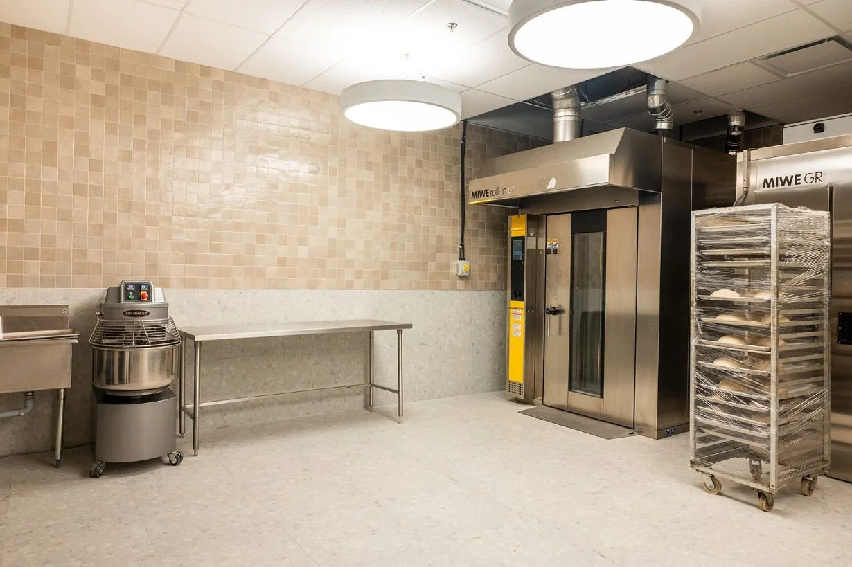 Commercial bakery kitchen with walk in oven, stainless steel equipment, and terrazzo tile floor and zellige tile walls