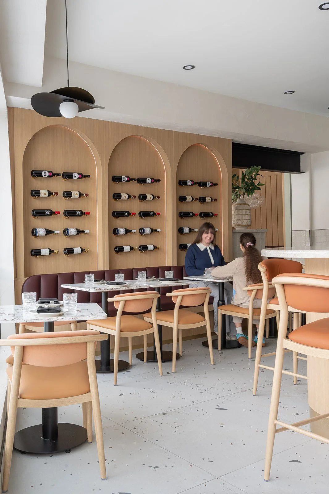 Italian restaurant featuring burgundy leather banquette, wine bottle display, and terrazzo flooring