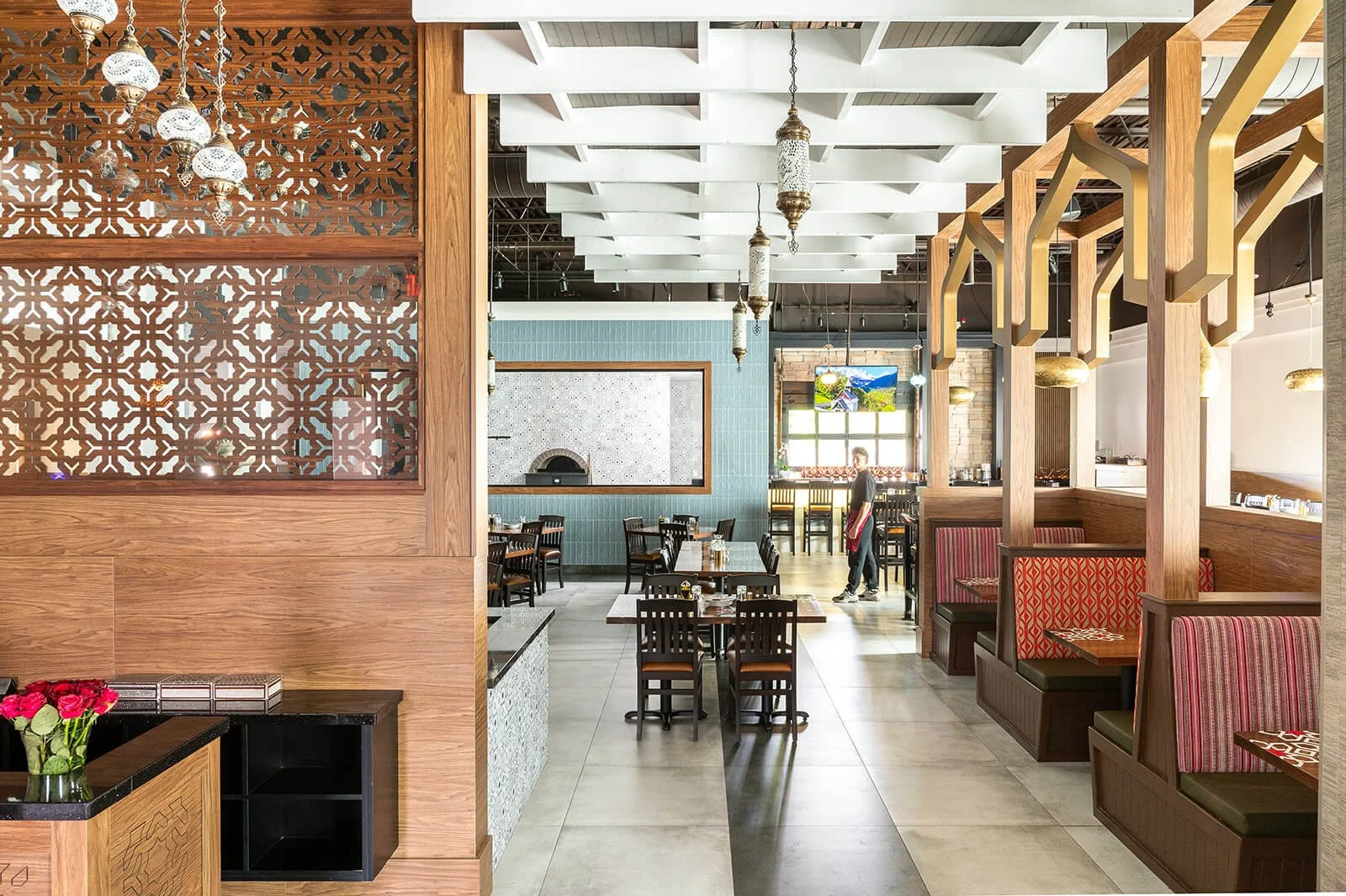 Middle Eastern restaurant with ornate wood arches and acccents leading towards a blue tiled wall with a window looking at a beautiful pizza oven