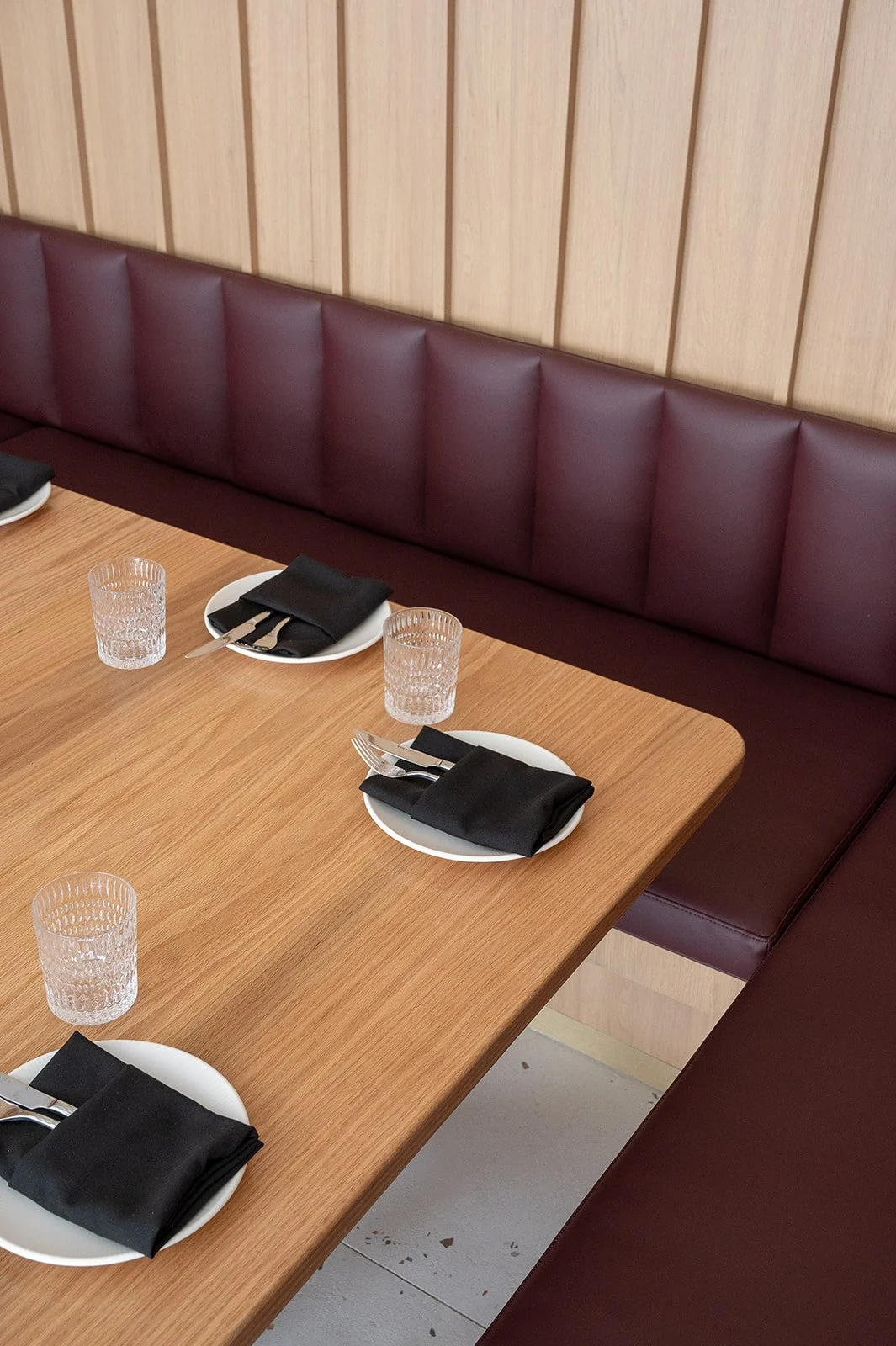 U-shaped booth in Italian restaurant featuring white oak vertical paneled walls, burgundy leather fabric, and white oak table top