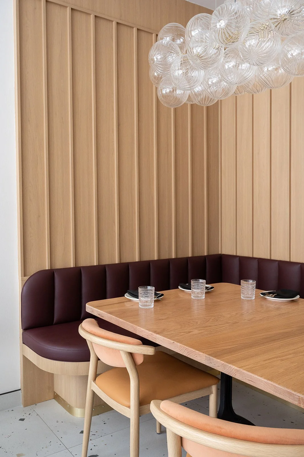 U-shaped booth in Italian restaurant featuring white oak vertical paneled walls, burgundy leather fabric, and glass bubble pendant above