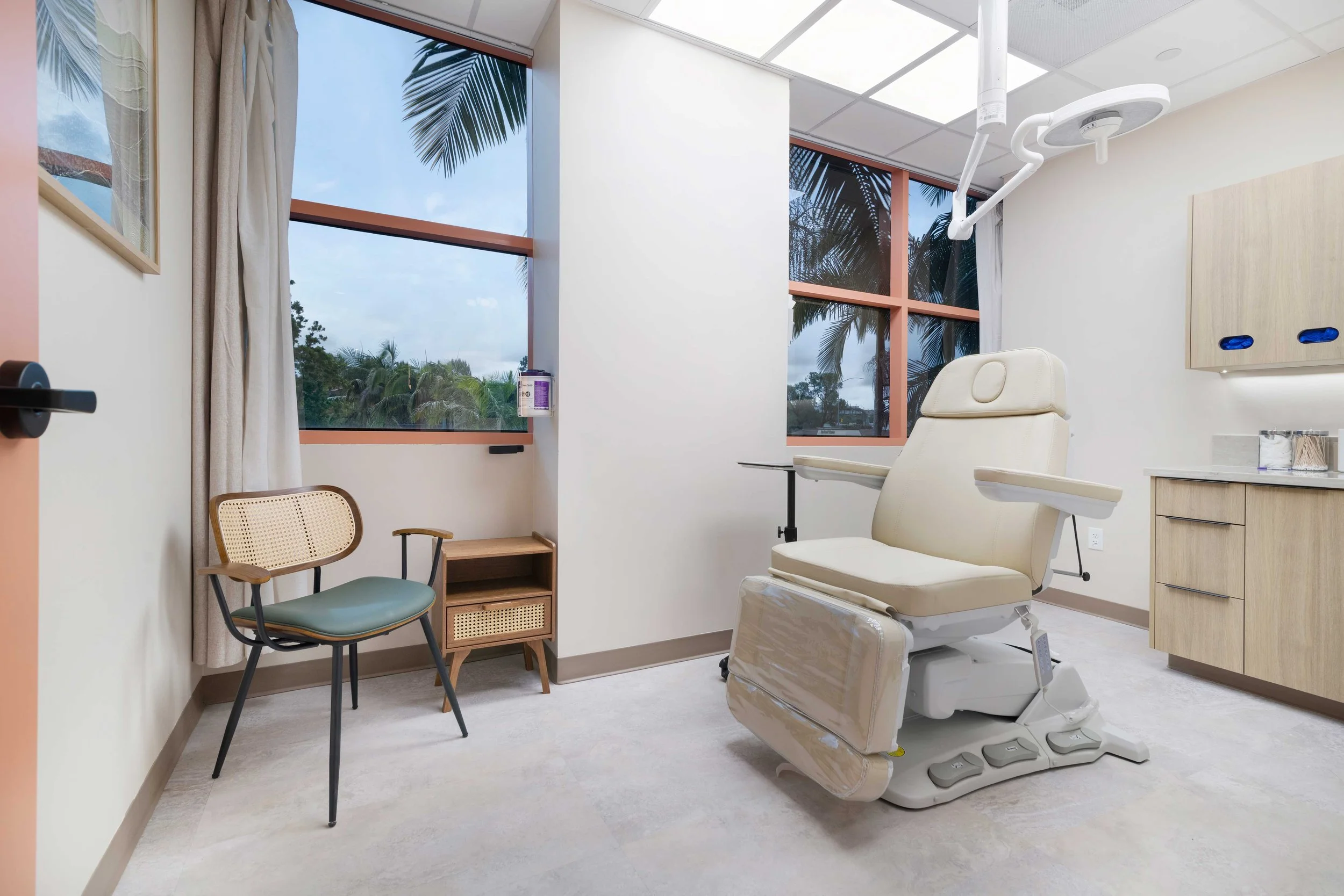 Bright, fully equipped dermatology exam room at Aliso Dermatology featuring a modern patient treatment chair and large windows