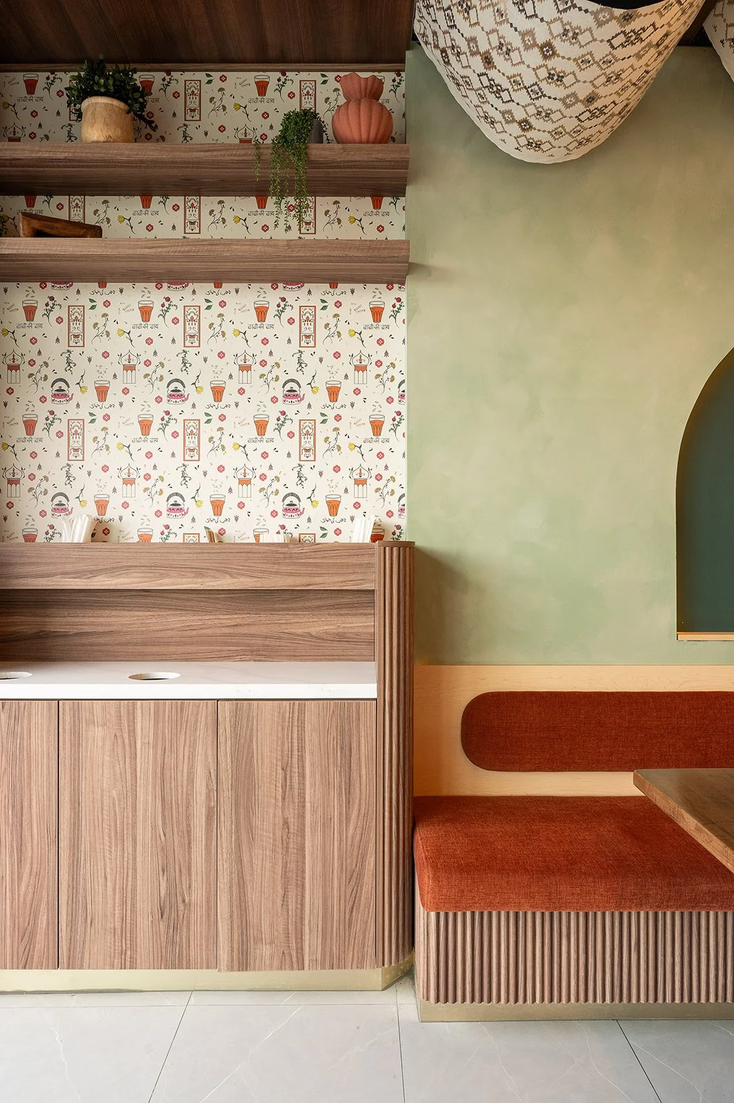 Cafe condiment station featuring wood cabinetry, floating shelves, and custom Indian-themed wallpaper decorated with chai glasses and teapots.