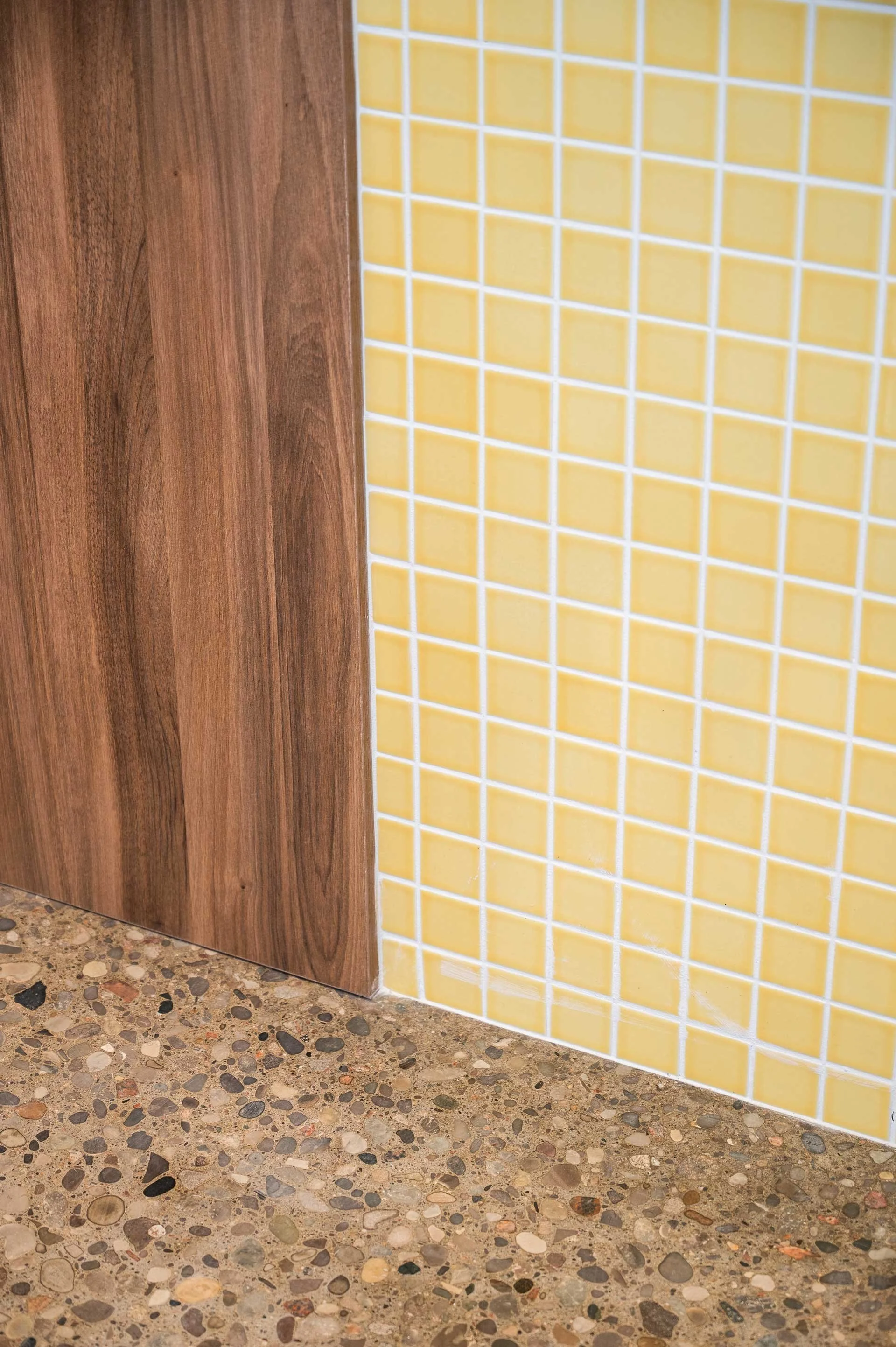 Wood wall cladding next to Yellow 2 inch square mosaic tiles on a wall that meet a texture poured concrete floor