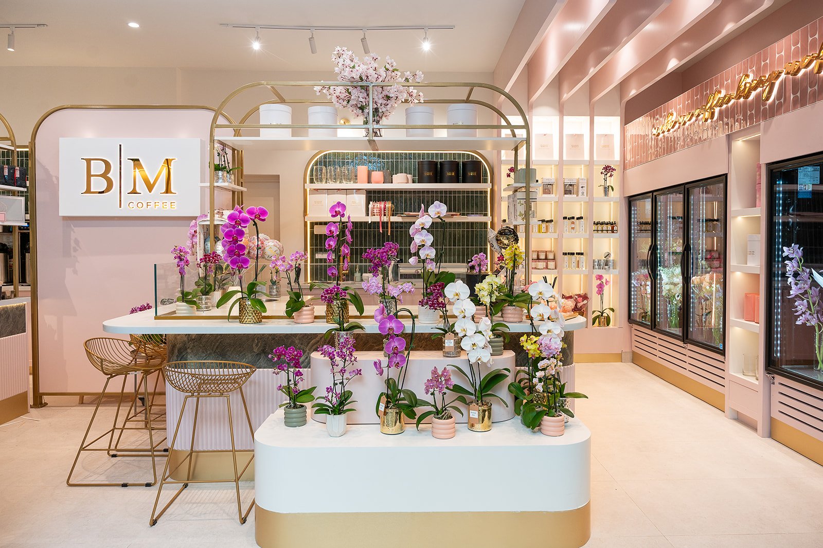 Floral retail display with orchid arrangements under the BM Coffee gold arch signage at Blossom Moments Scotia Plaza