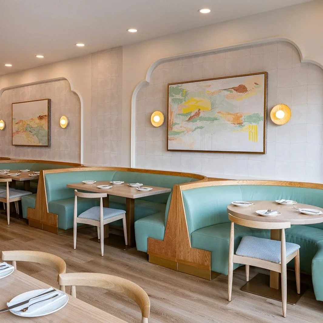 Modern Mediterranean restaurant interior design in Oakville featuring custom artwork, curved banquette seating, blue upholstery, and warm lighting
