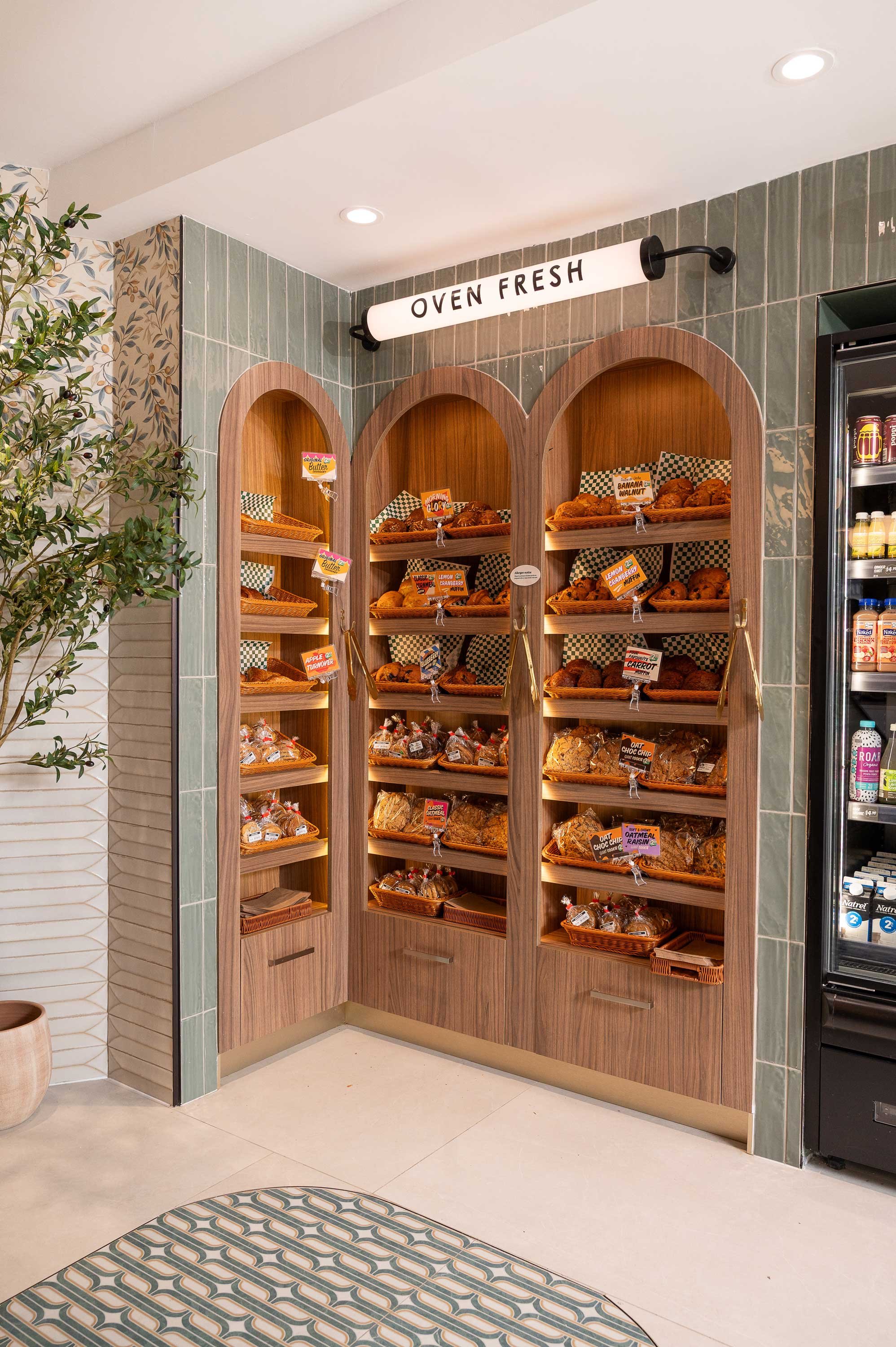 Light walnut arched bakery displays recessed into sage green tile wall