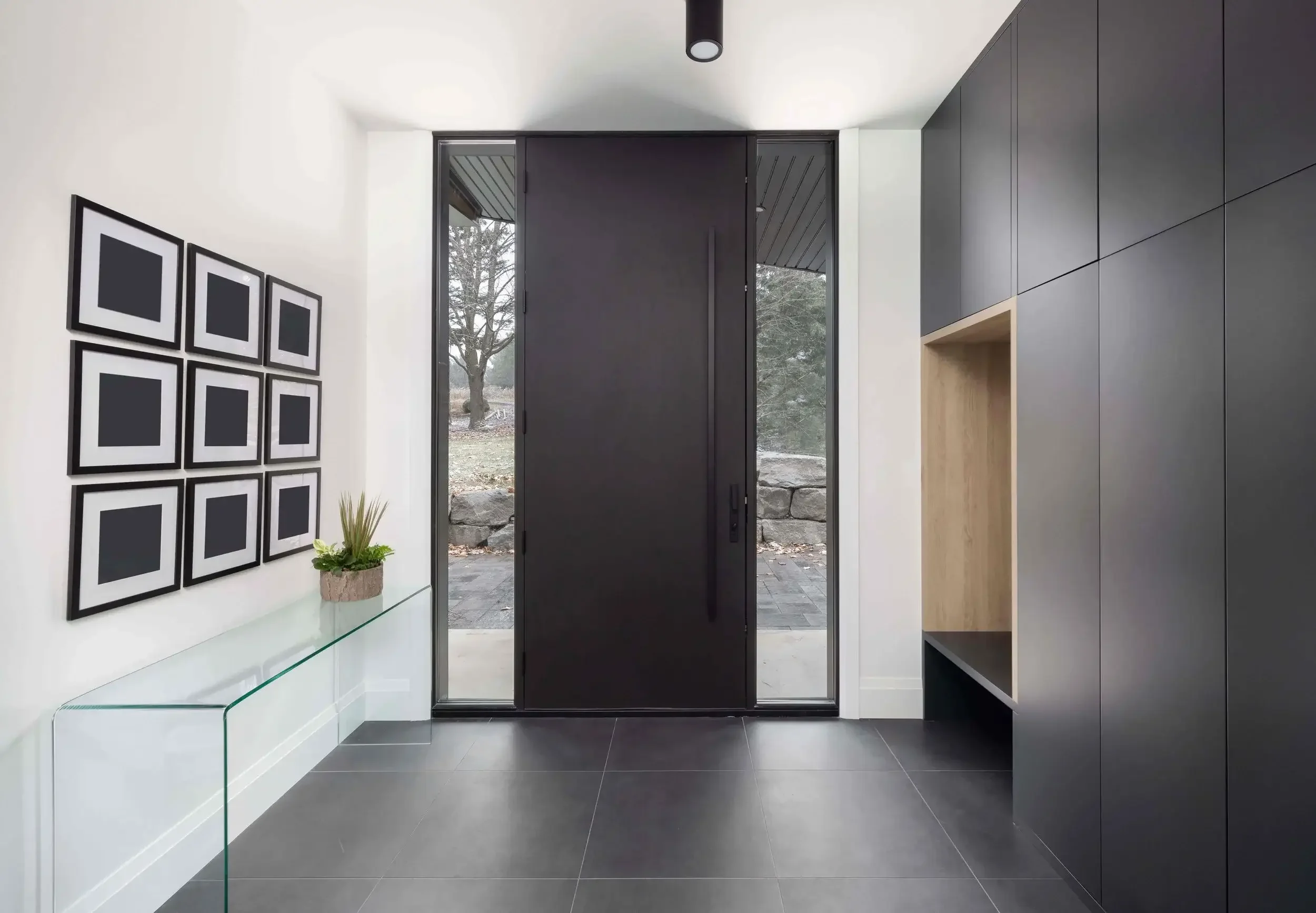 Modern foyer entryway design in East Gwillimbury custom home featuring black front door, built-in storage, and minimalist interior layout