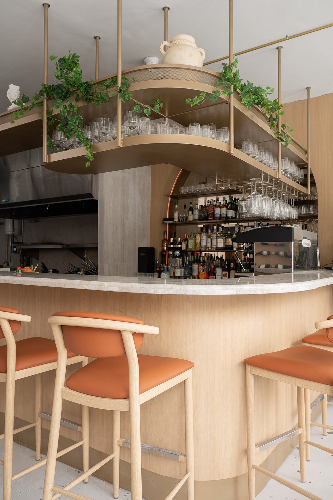 Restaurant bar with overhead brass glass display, quartz counters, and white oak bar face