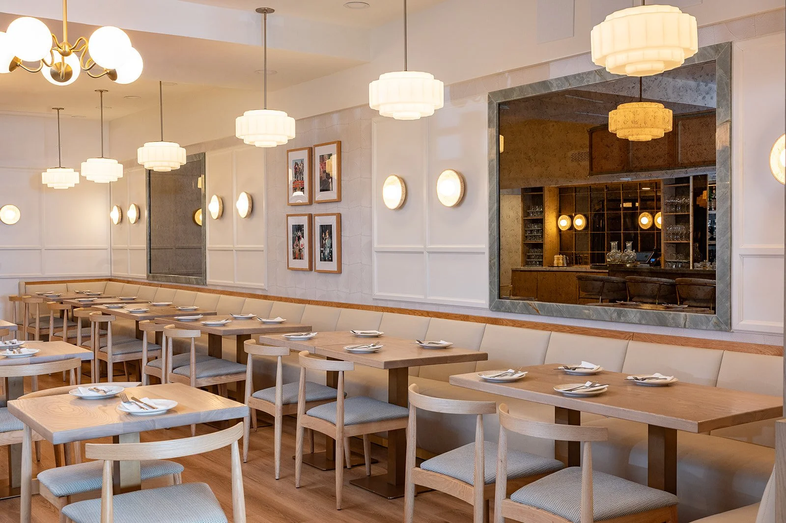 Tabule Oakville restaurant interior design — dining room with banquette seating, framed artwork, brass pendants, and bar view designed by Sansa Interiors