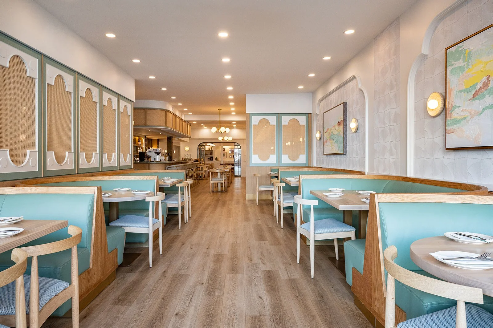 Dining room at Tabule Middle Eastern Cuisine in Oakville with teal booth seating, arched cane-panel dividers, a gallery wall of framed art, and a pendant chandelier over the main aisle
