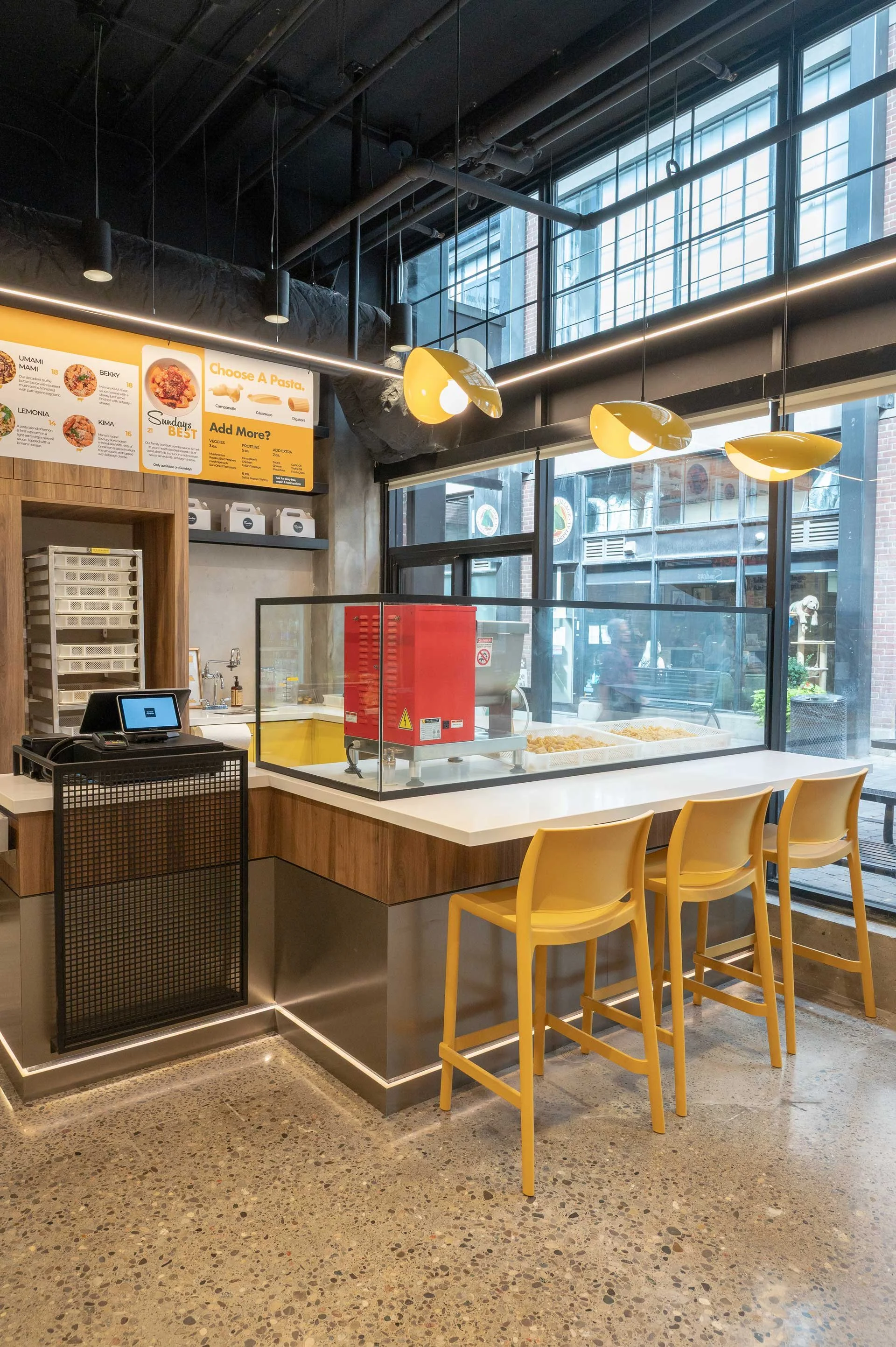 3 yellow bar stools at a pasta restaurant counter with 3 yellow pasta shaped pendant lights