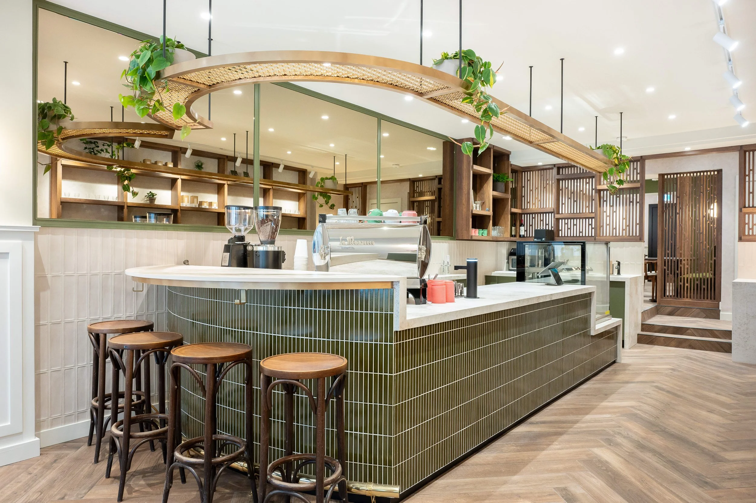 Curved rattan and brass service counter with trailing greenery above the espresso bar at Black Canary café, designed by Sansa Interiors in Toronto