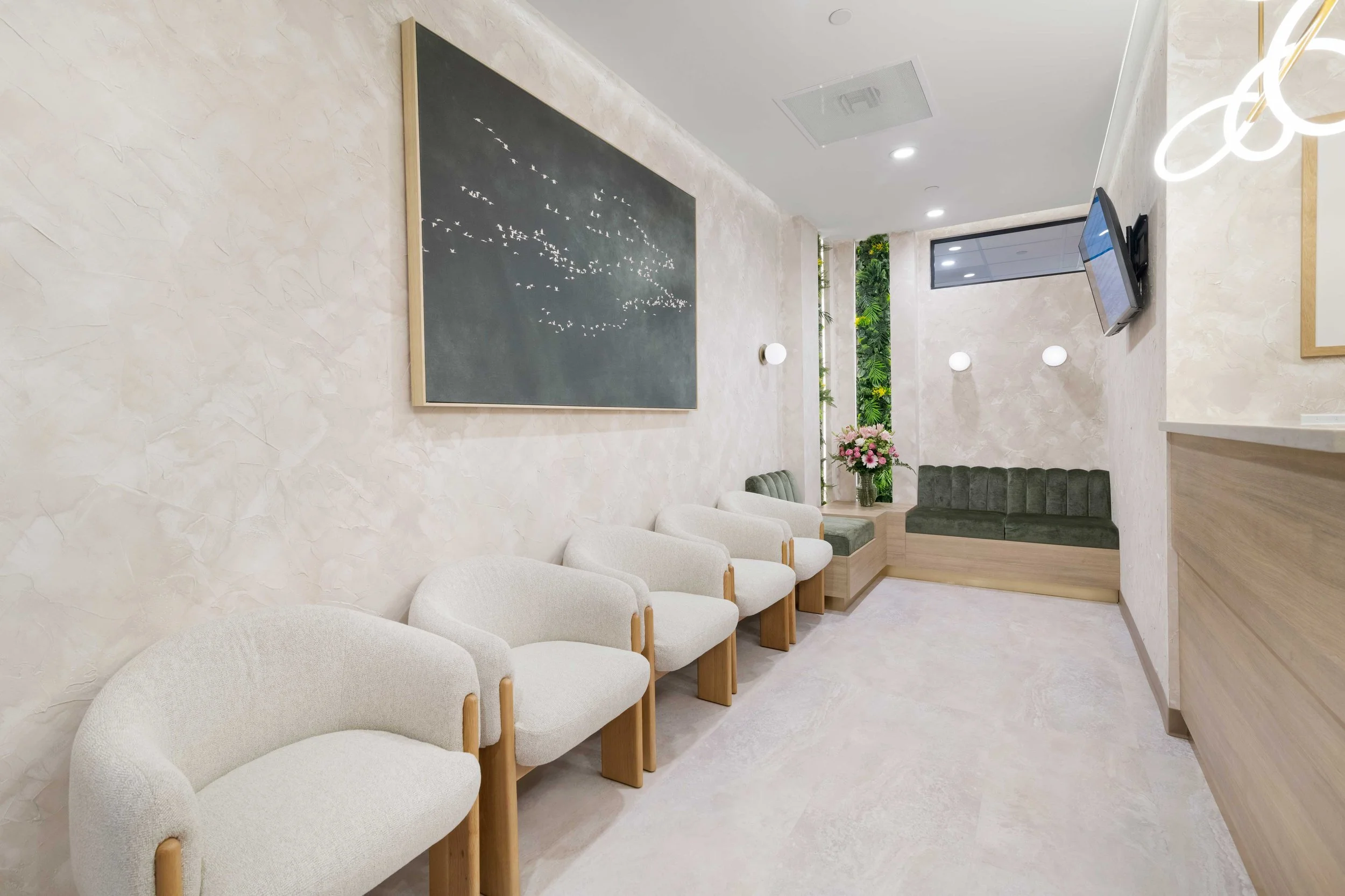 Modern waiting room at Aliso Dermatology featuring comfortable white textured chairs with wood frames, elegant wall art, and a relaxing atmosphere.
