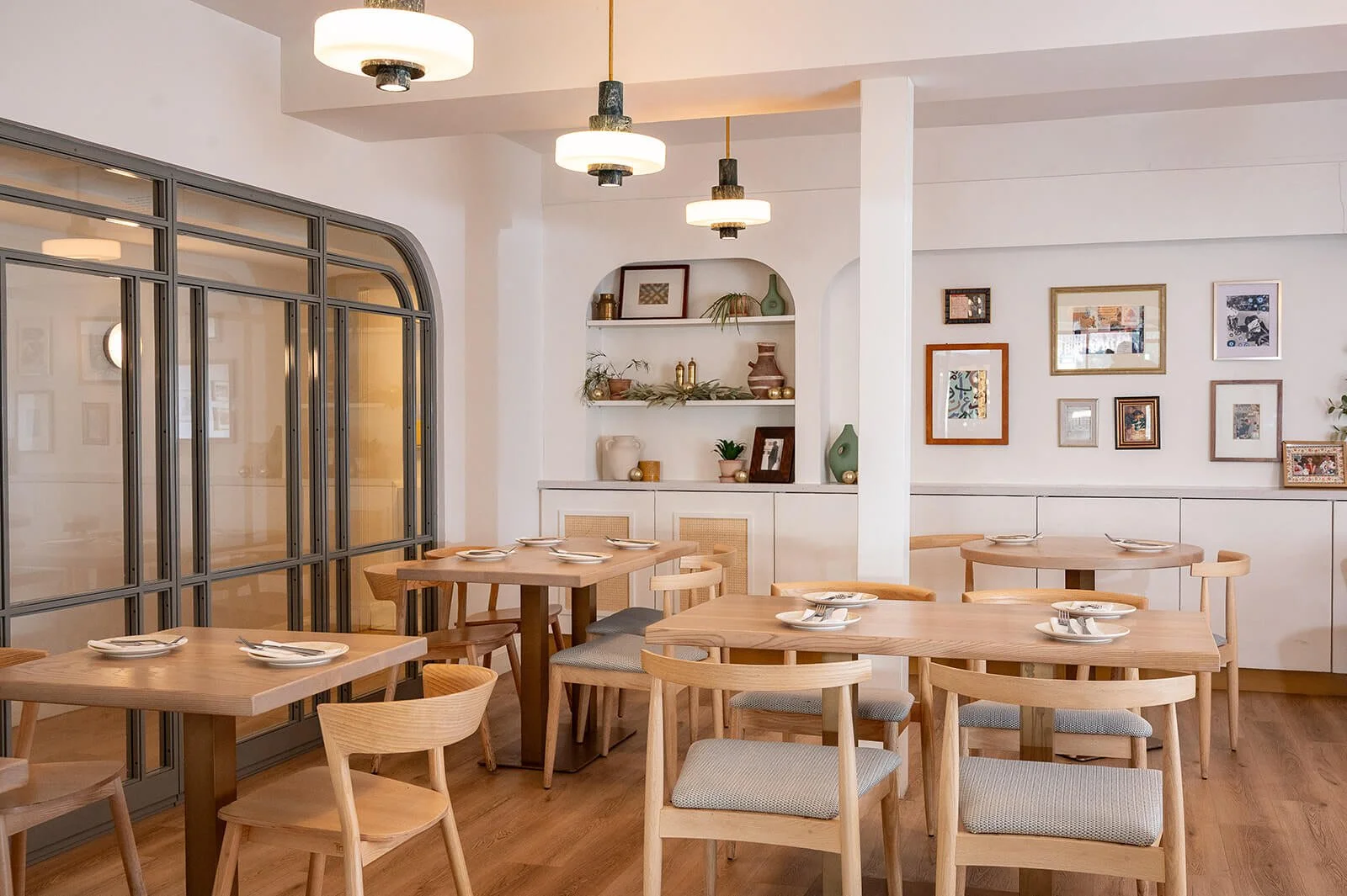 Tabule Oakville main dining room — wood tables, light woven chairs, and gallery wall by Sansa Interiors