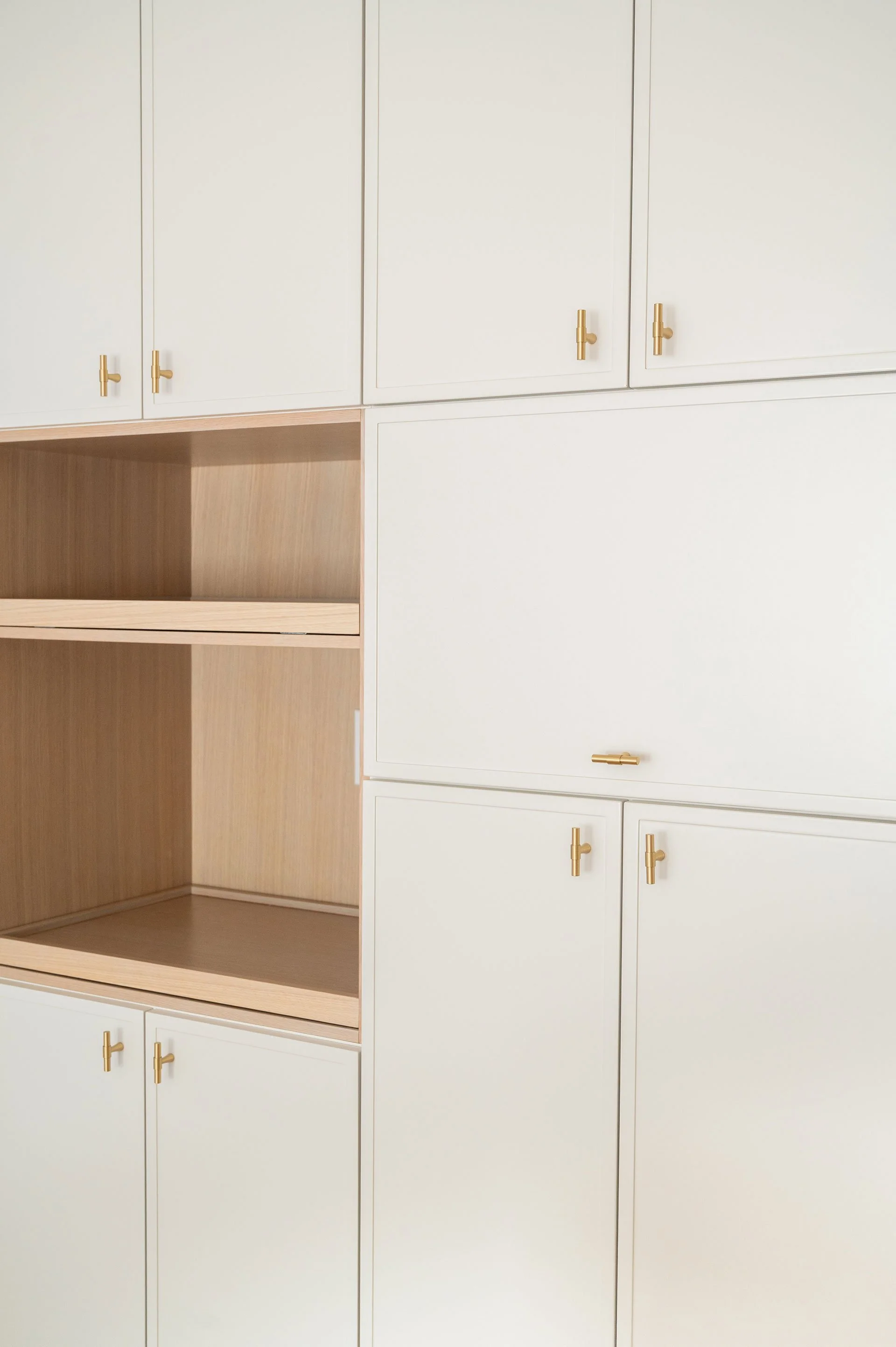 Full height cream slim shaker cabinetry with a peak a boo white oak opening for appliances