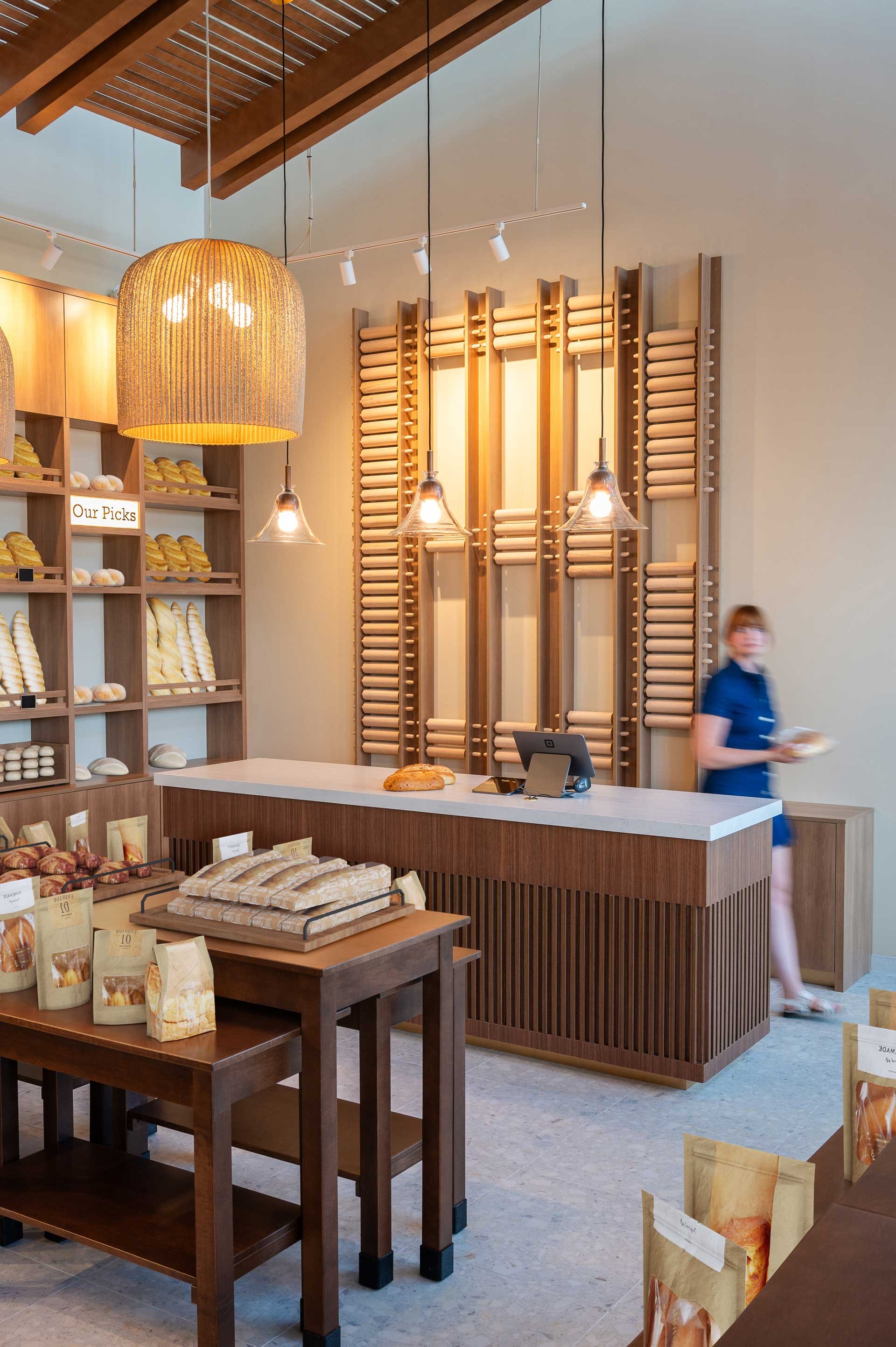 Woman holding bread behind bakery custom check out counter with wood slats with custom rolling pin wall feature behind