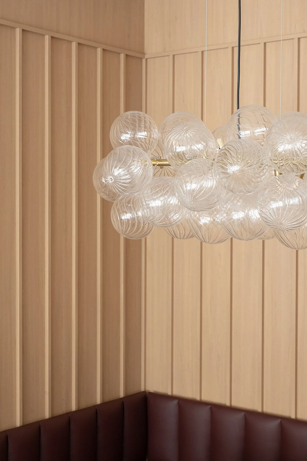 Glass bubble pendant in front of white oak vertical paneled wall 