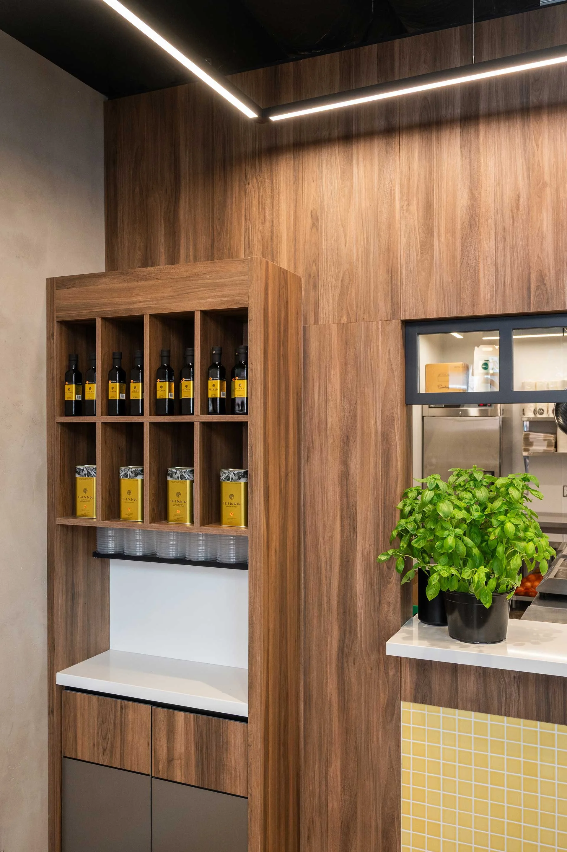 Condiment station counter with open shelves above housing various olive oil bottles, cladded with wood and stainless steel doors